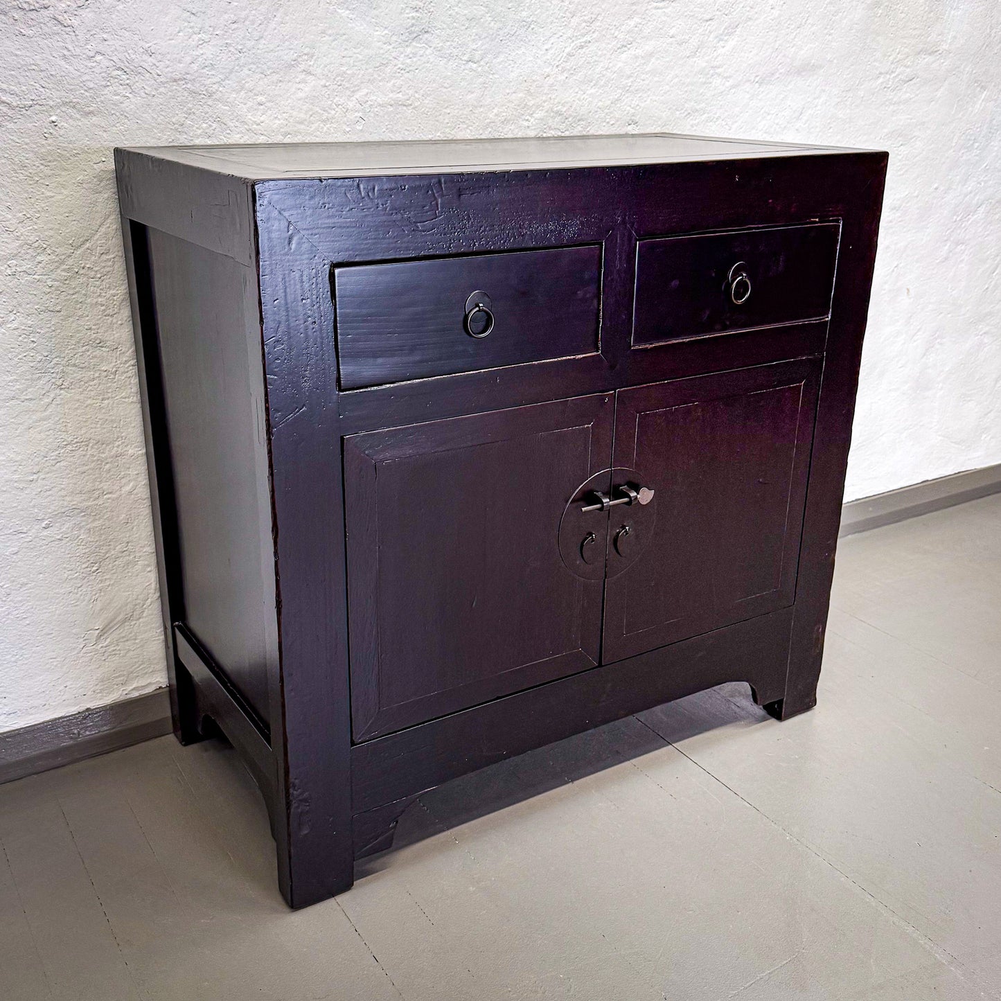 Dark wooden cabinet with two drawers and a door on a light floor and wall.