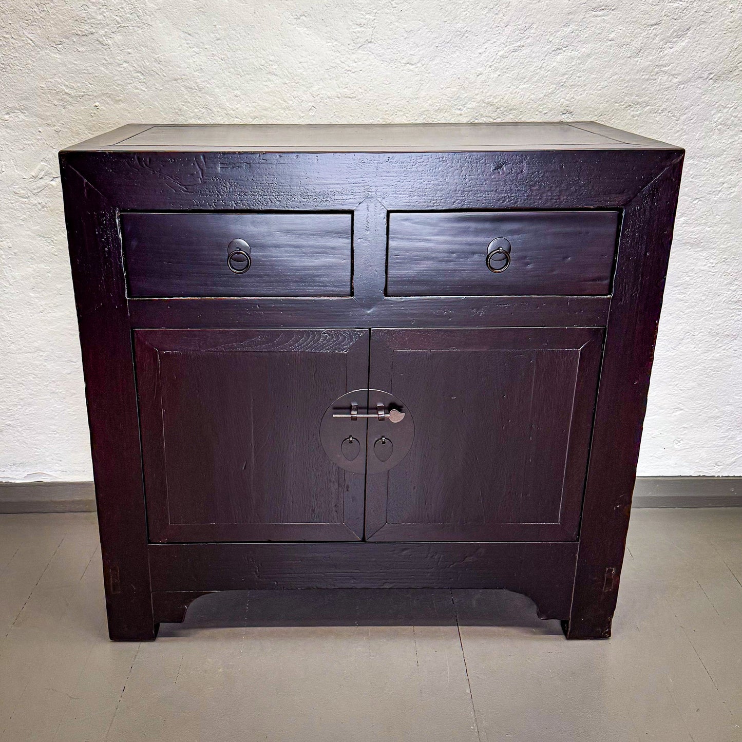 Dark wooden cabinet with two drawers and a door on a light gray background