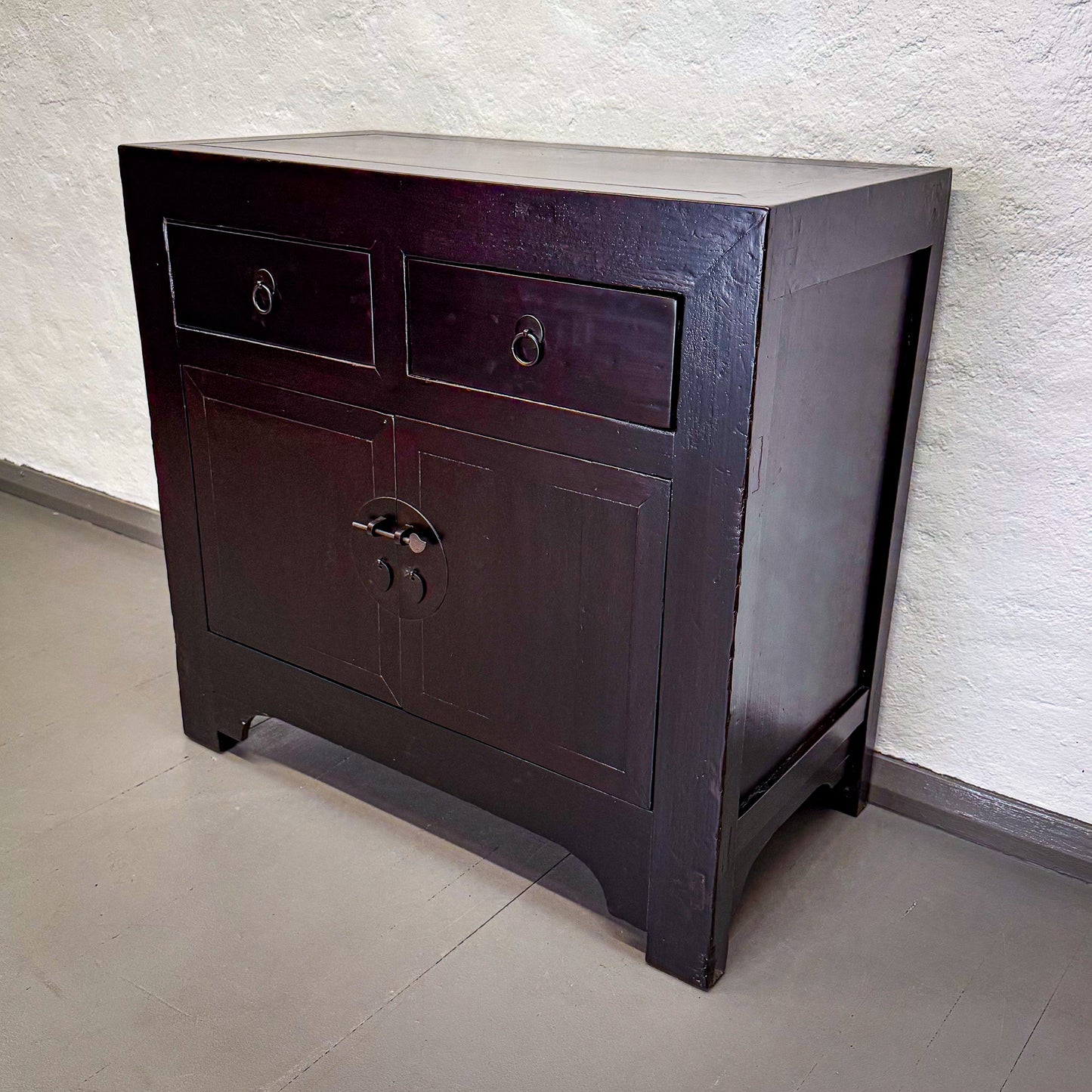 Dark wooden cabinet with two drawers against a light textured wall.