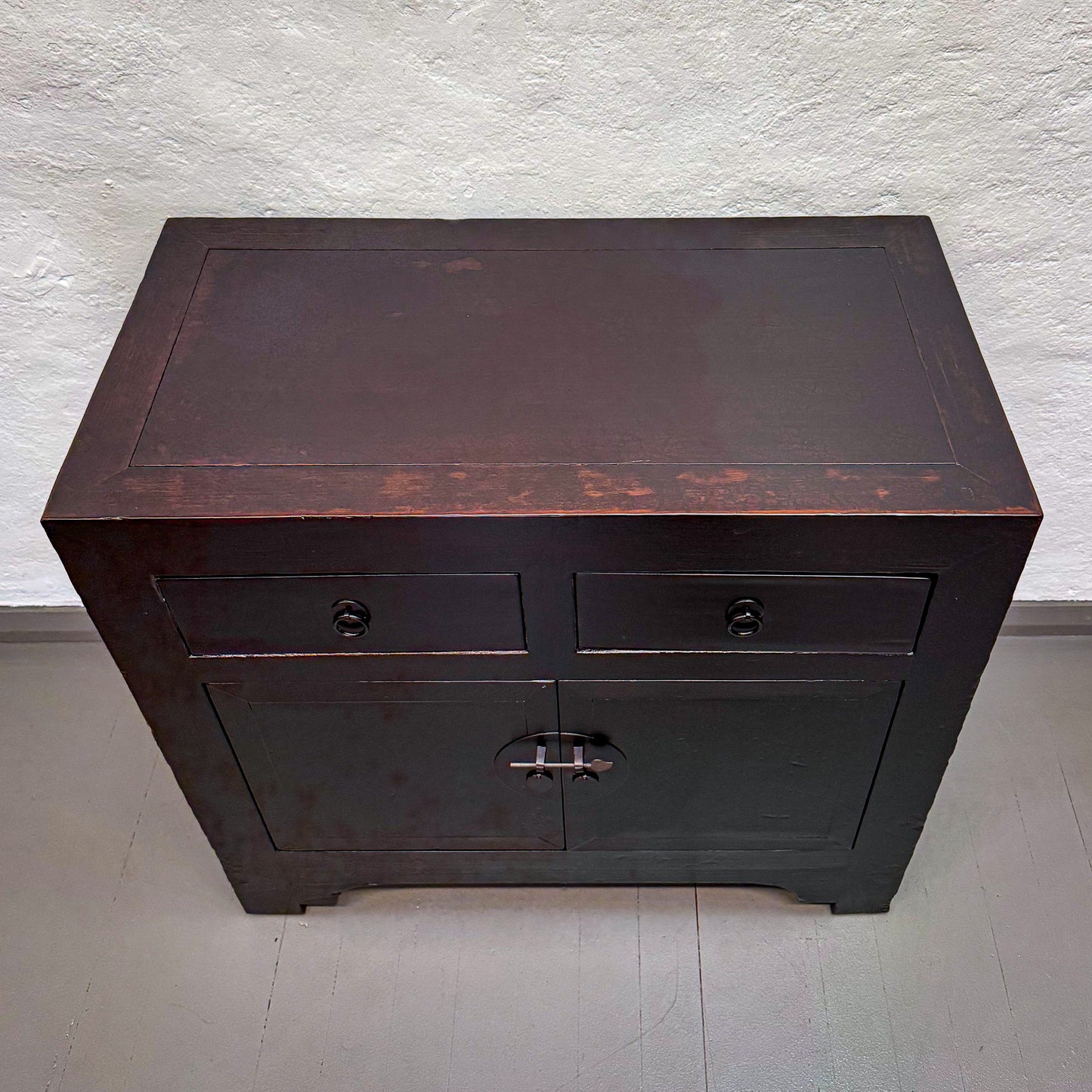 Dark wooden cabinet with two drawers against a light gray wall.