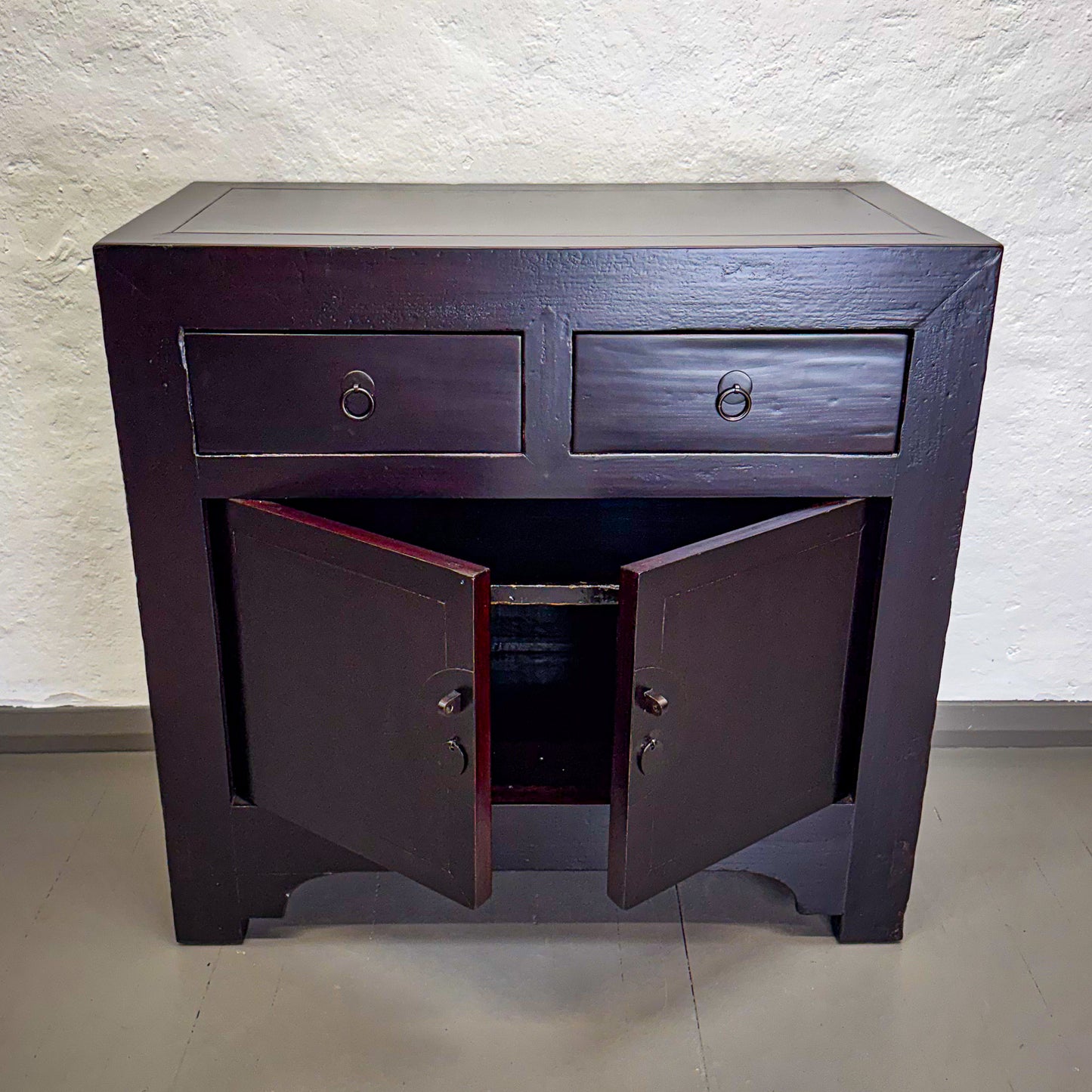 Dark wooden side table with two drawers and two doors against a light textured wall.