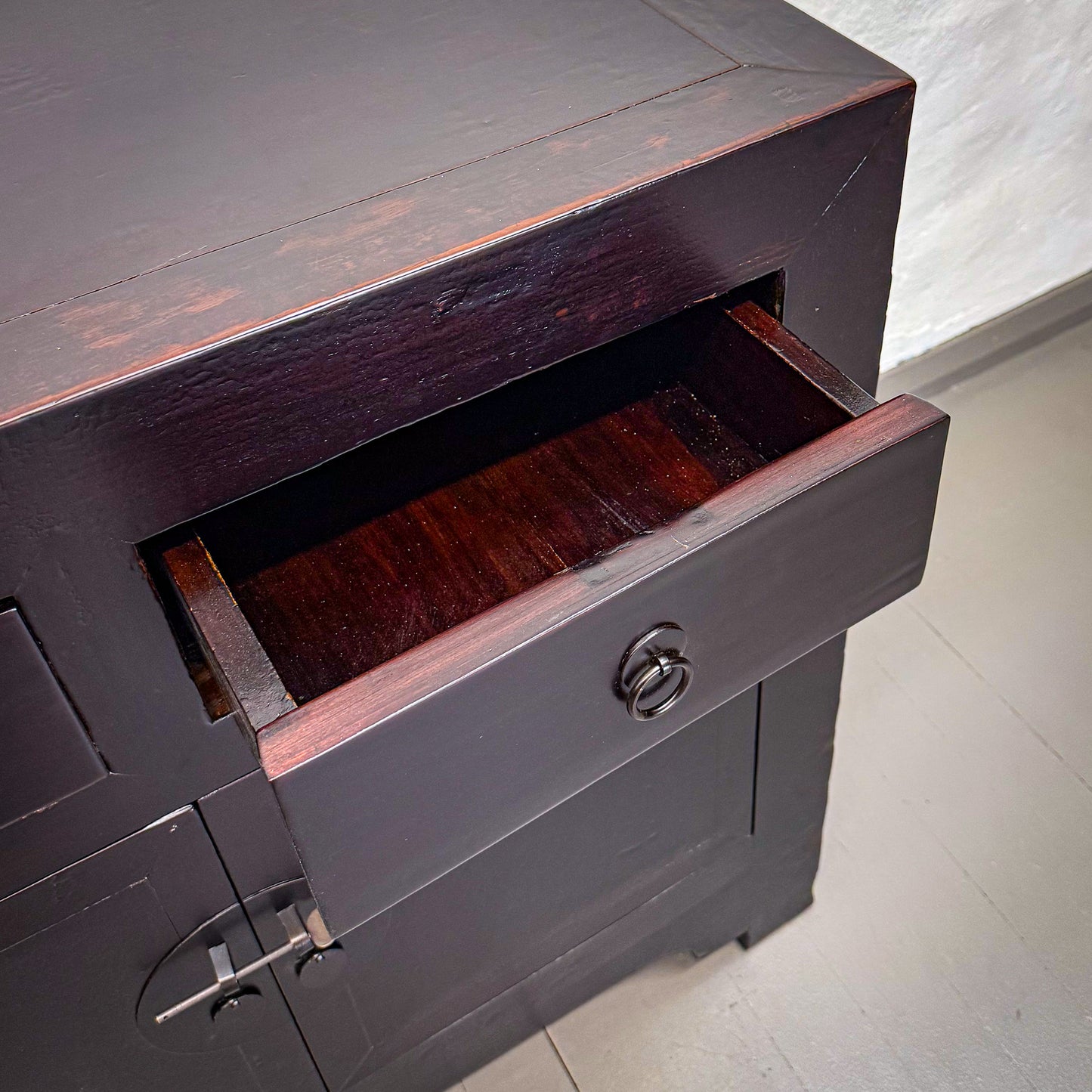 Dark wooden cabinet with an open drawer on a light gray floor.