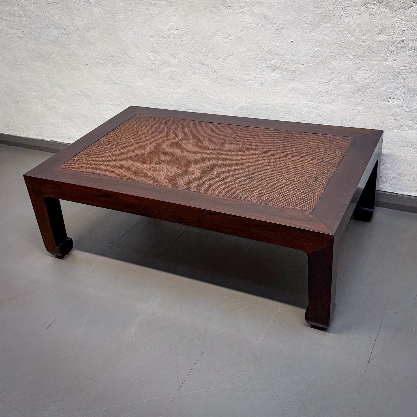 Wooden coffee table with woven top against a white textured wall.