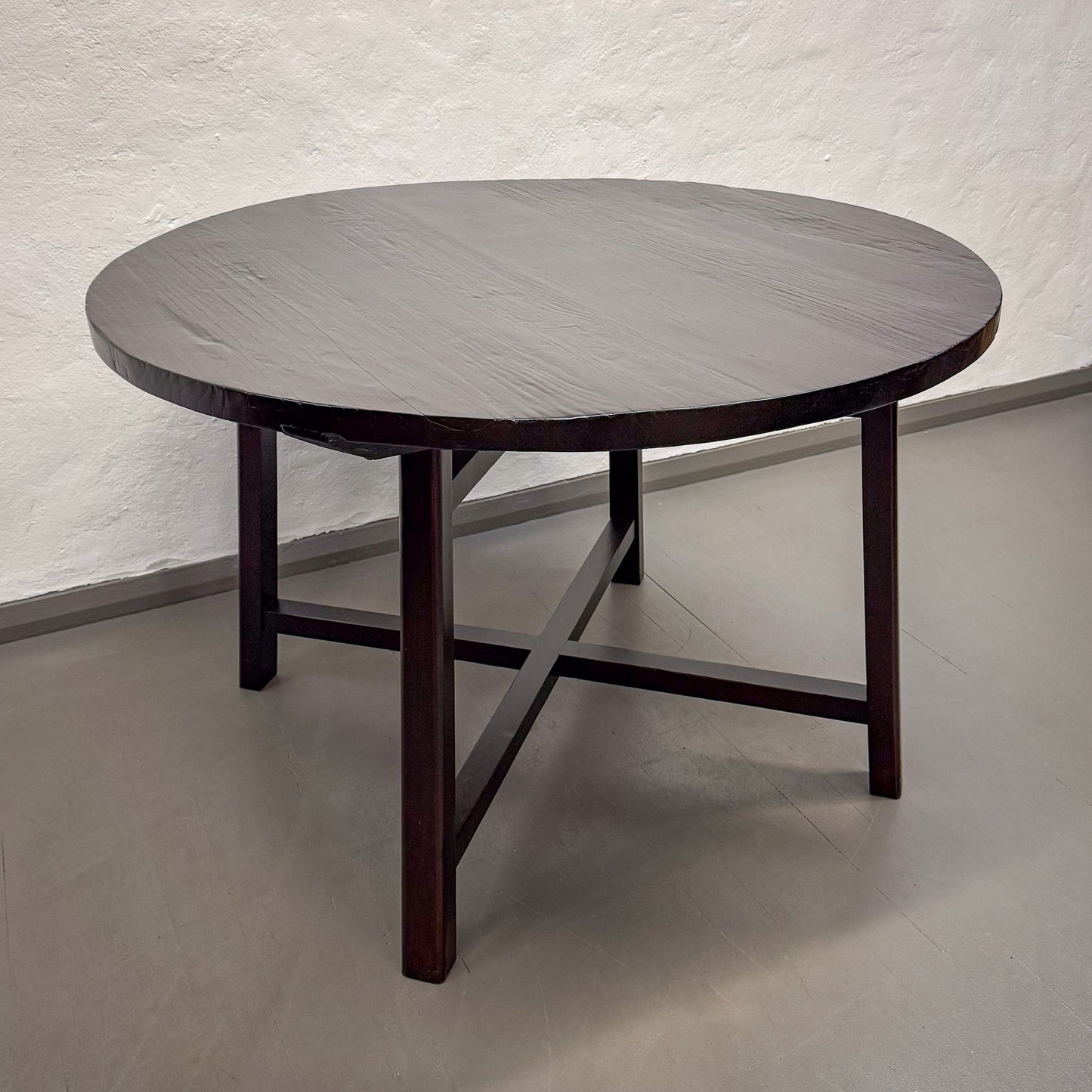 Round wooden table with a dark finish on a plain floor and wall background