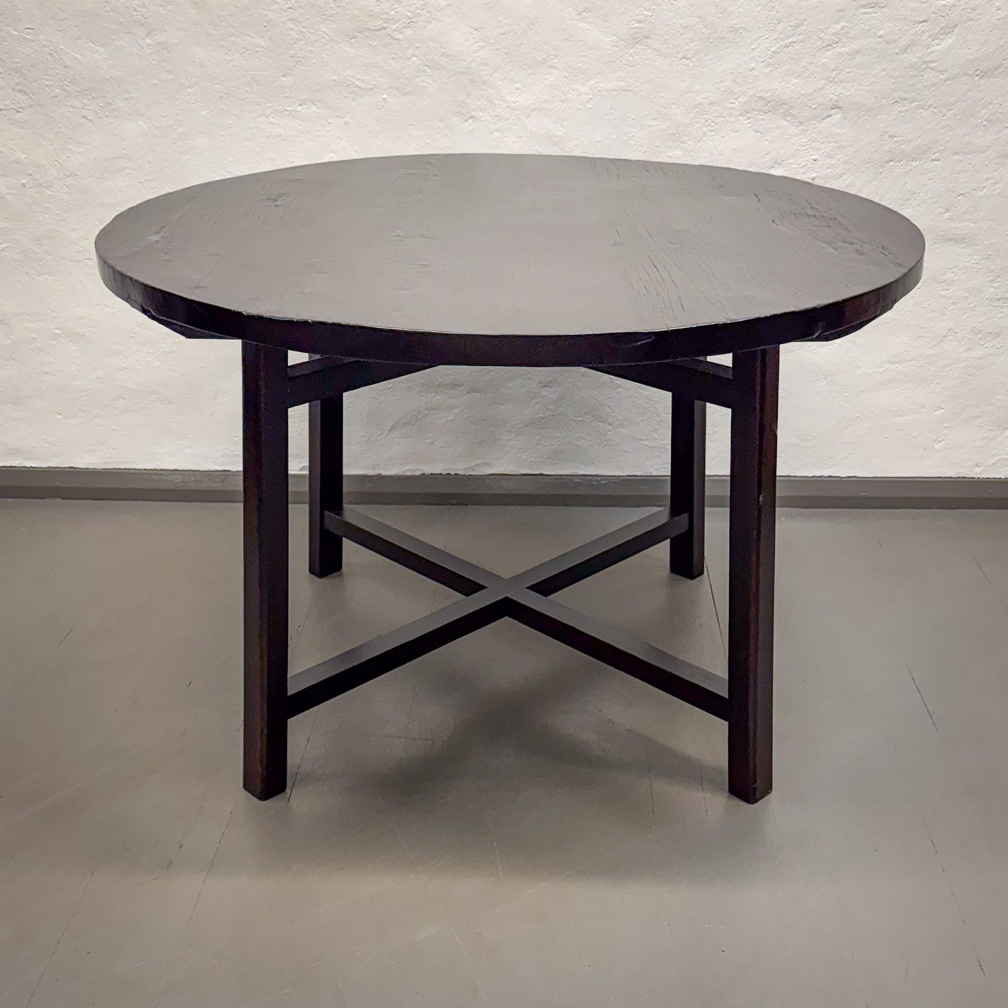 Round dark wooden table with a light gray floor and white textured wall background