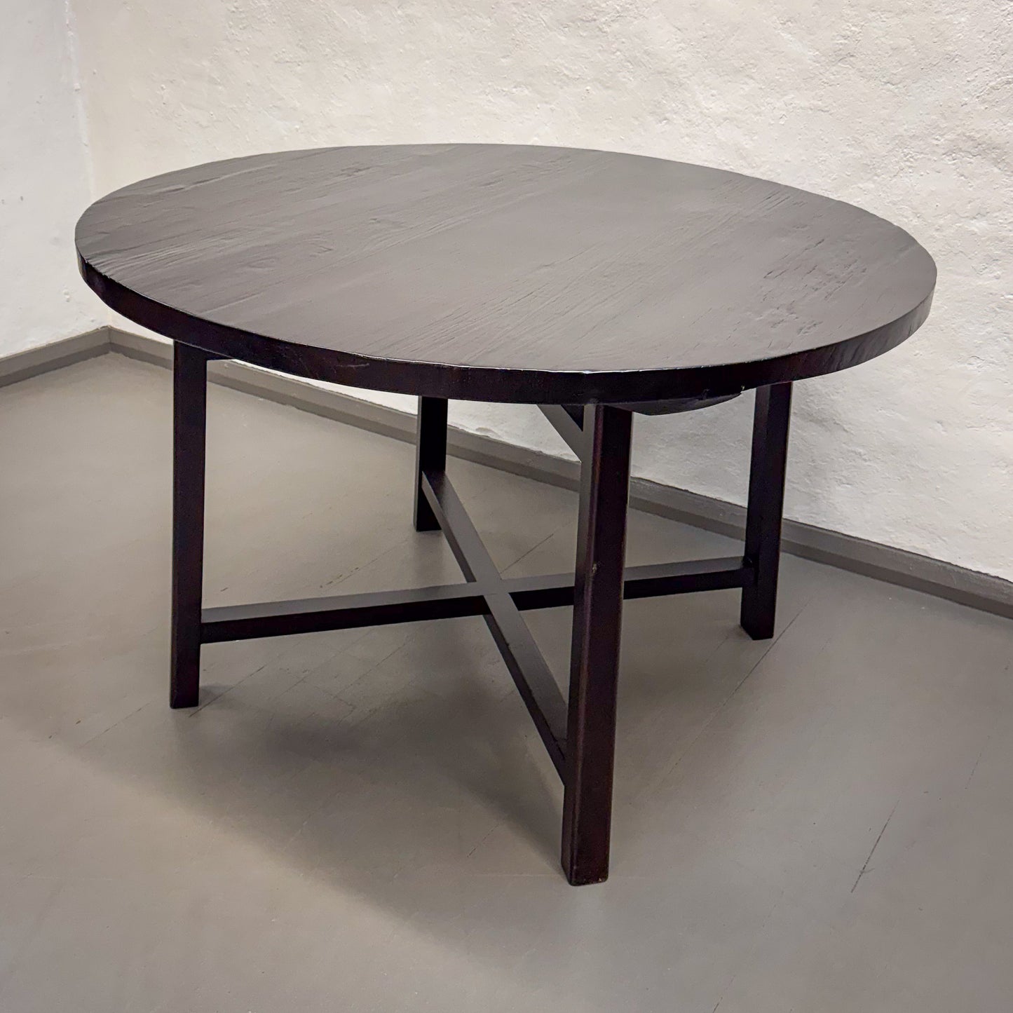 Round wooden table with a dark finish on a plain floor and wall background