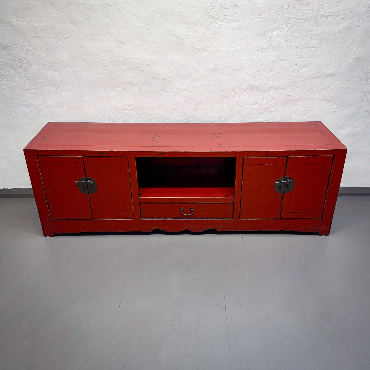 Red wooden TV stand against a white brick wall.