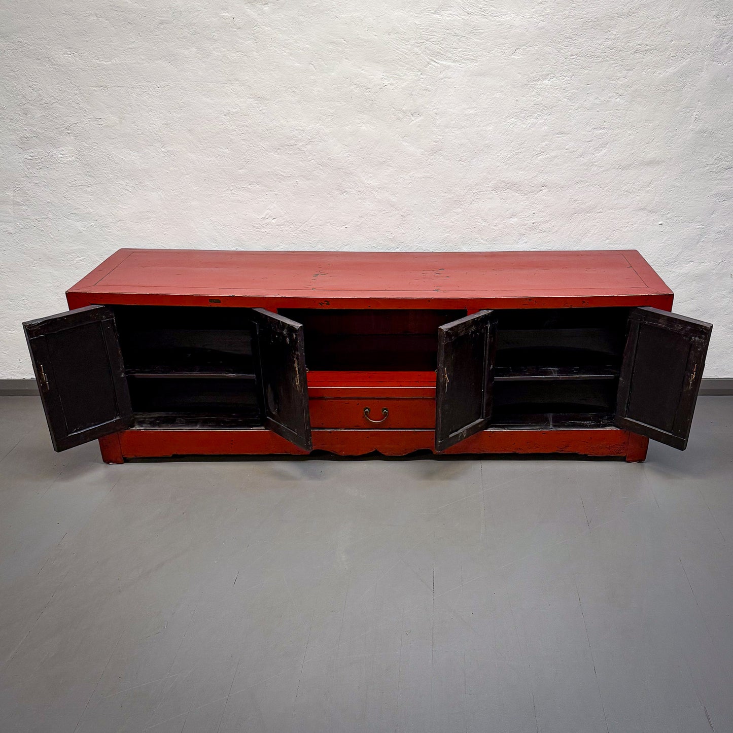 Red wooden cabinet with open doors on a gray floor against a white textured wall