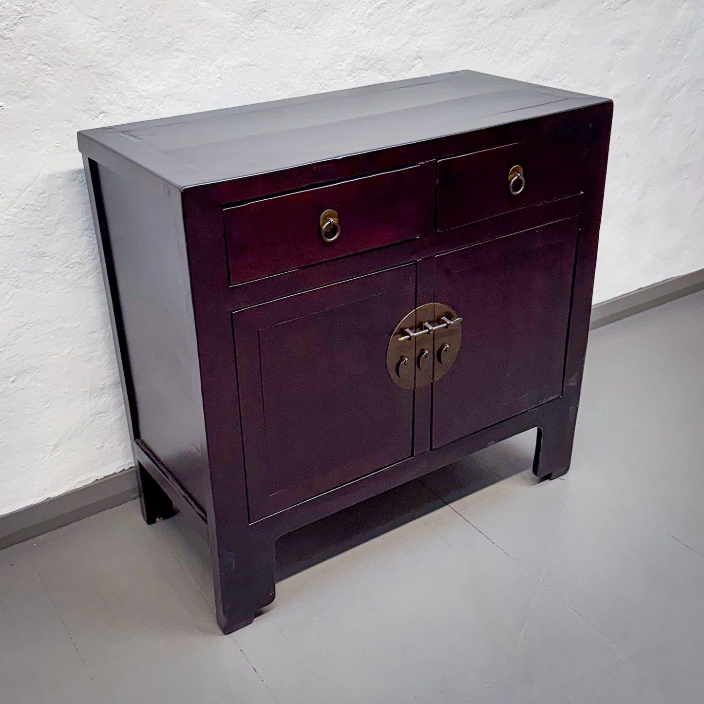 Wooden side table with a dark finish and brass hardware against a white wall.