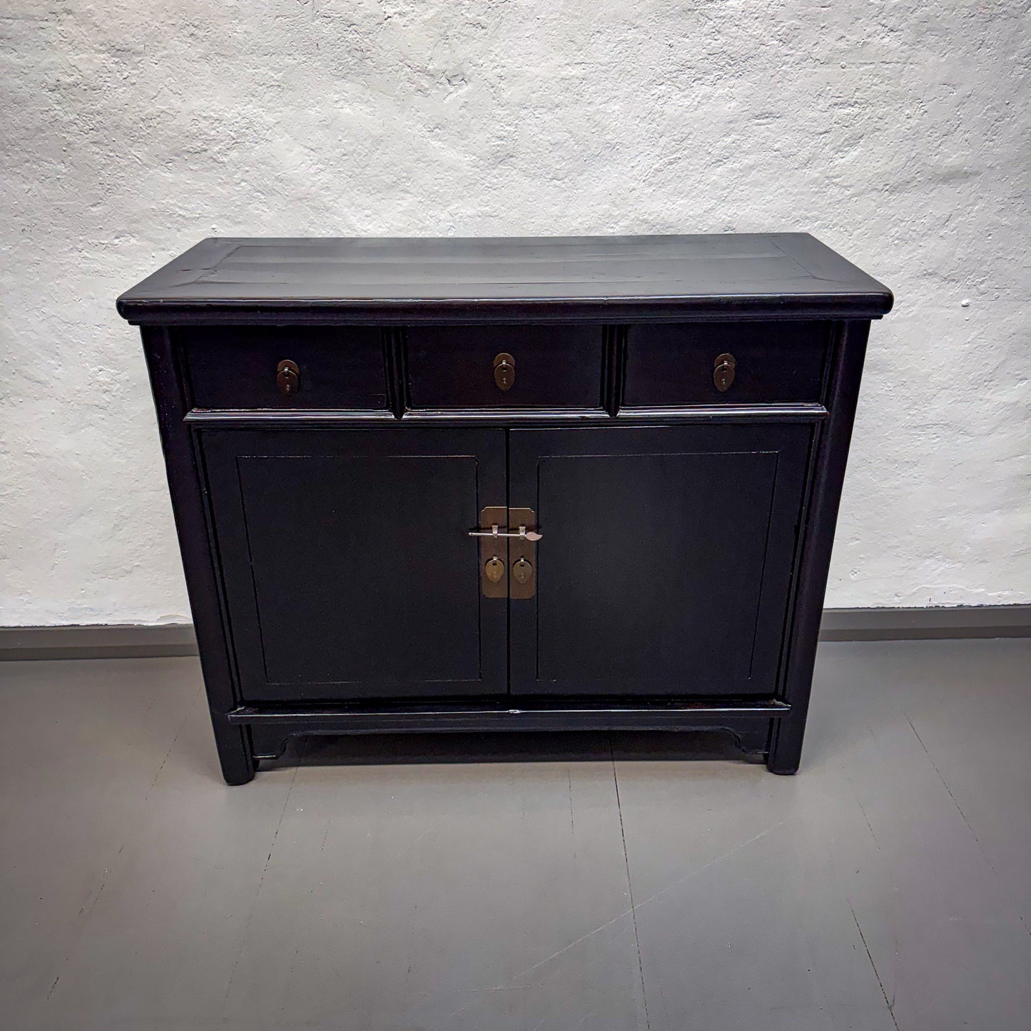 Black wooden cabinet with two doors and two drawers against a white wall.