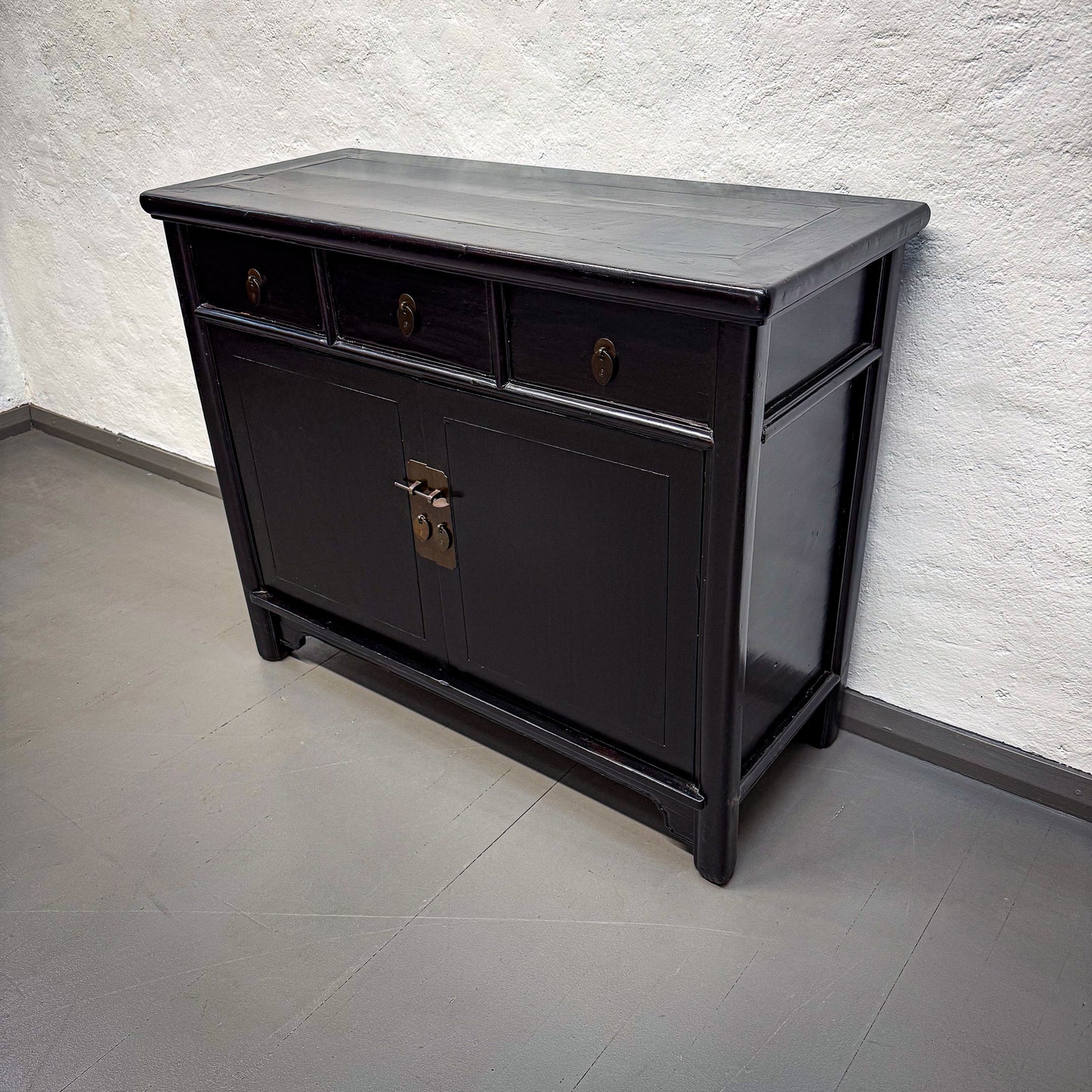 Black wooden sideboard with a textured wall and gray floor in the background