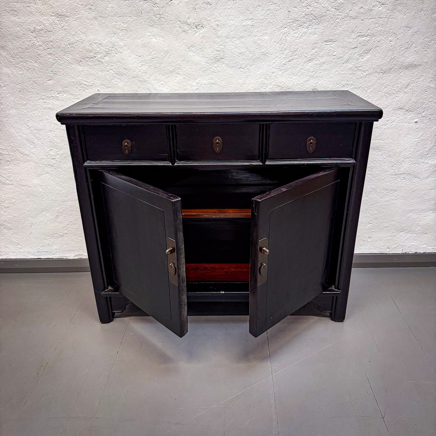 Black wooden sideboard with open doors against a white textured wall.