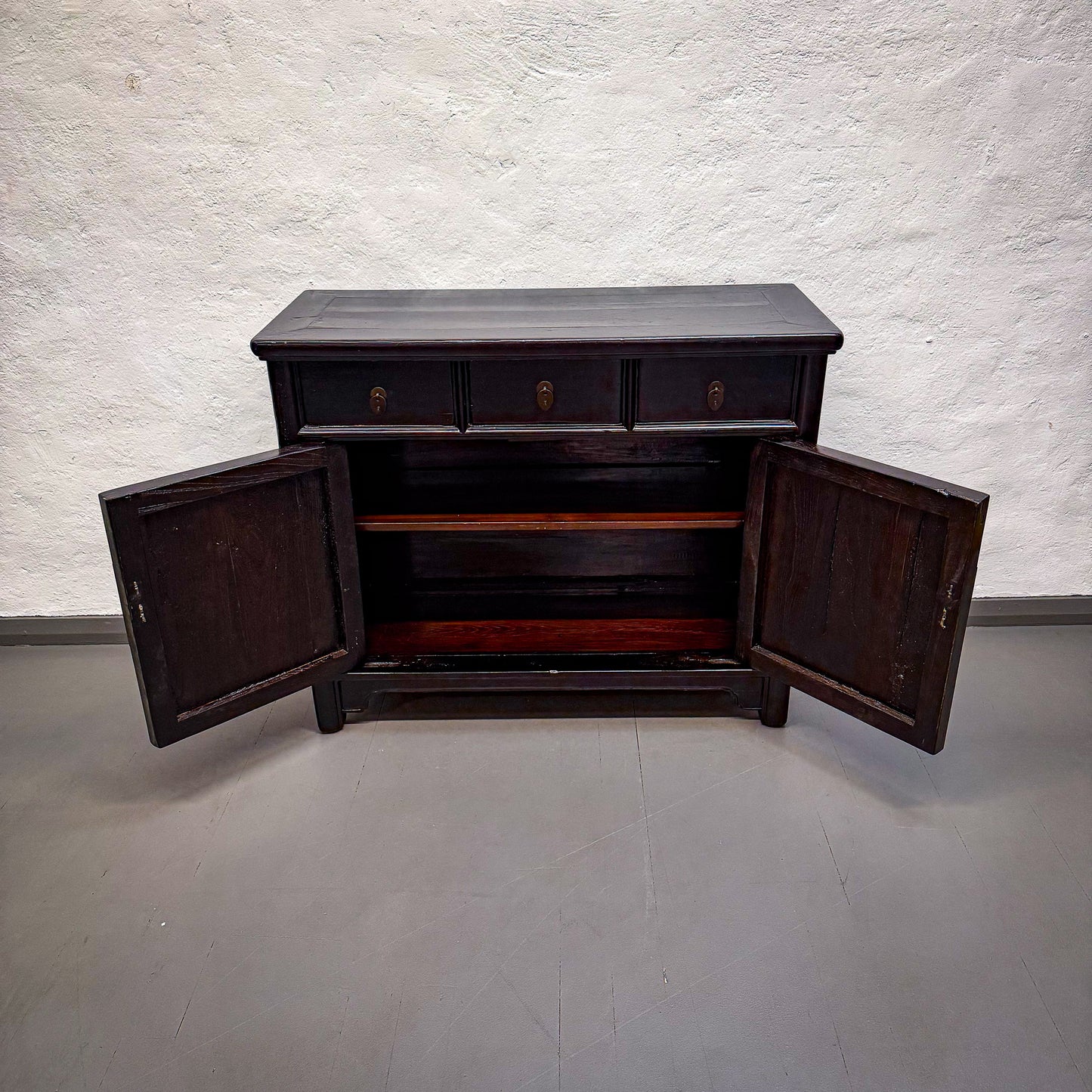Dark wooden cabinet with open doors on a plain floor and wall background