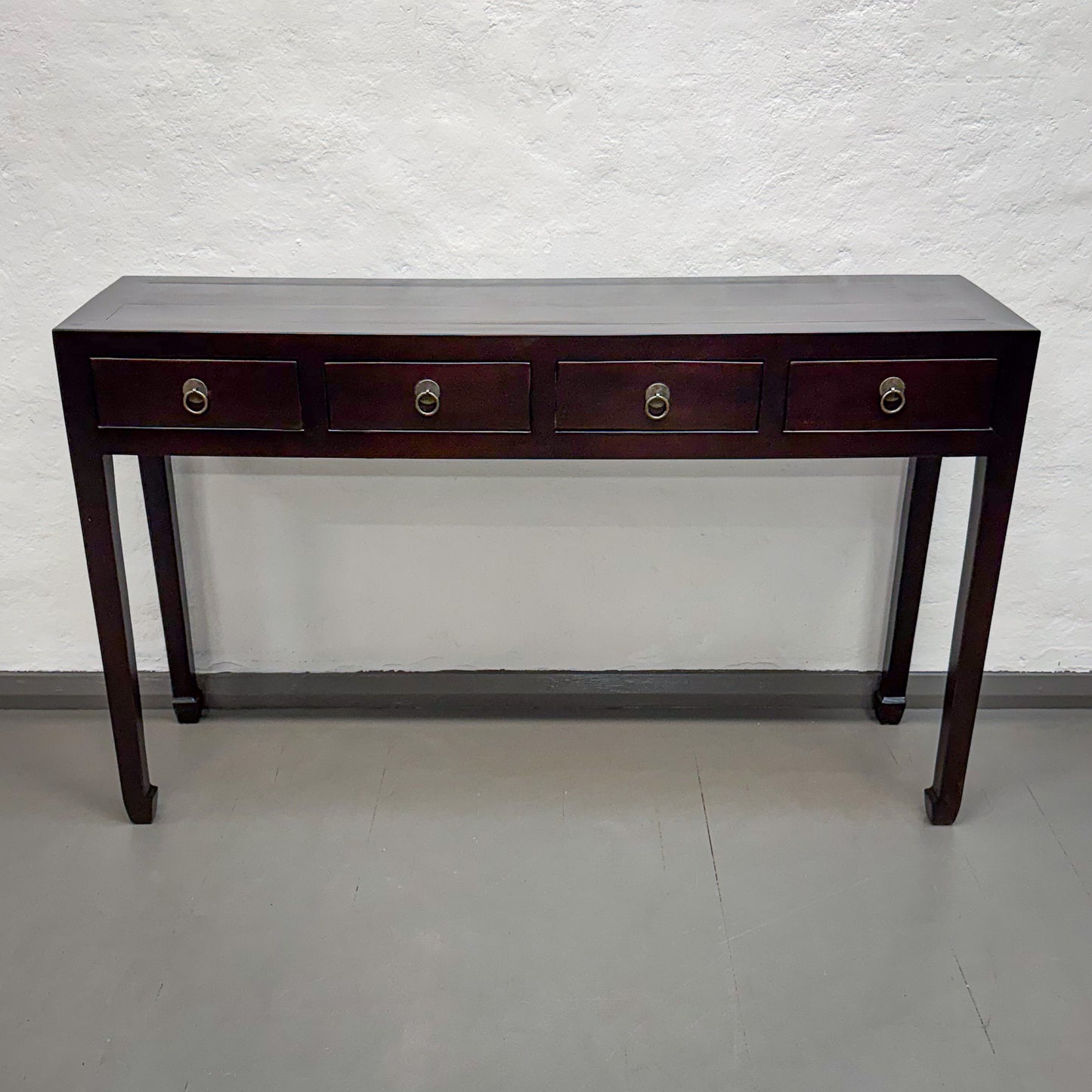 Wooden console table with four drawers against a white wall.