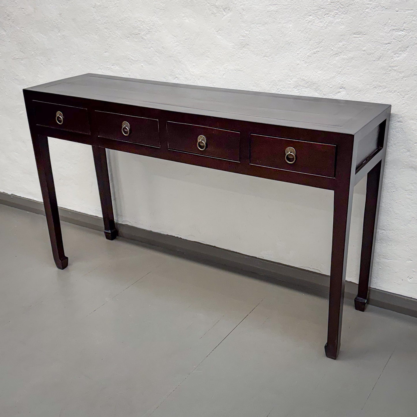 Wooden console table with four drawers against a white brick wall.
