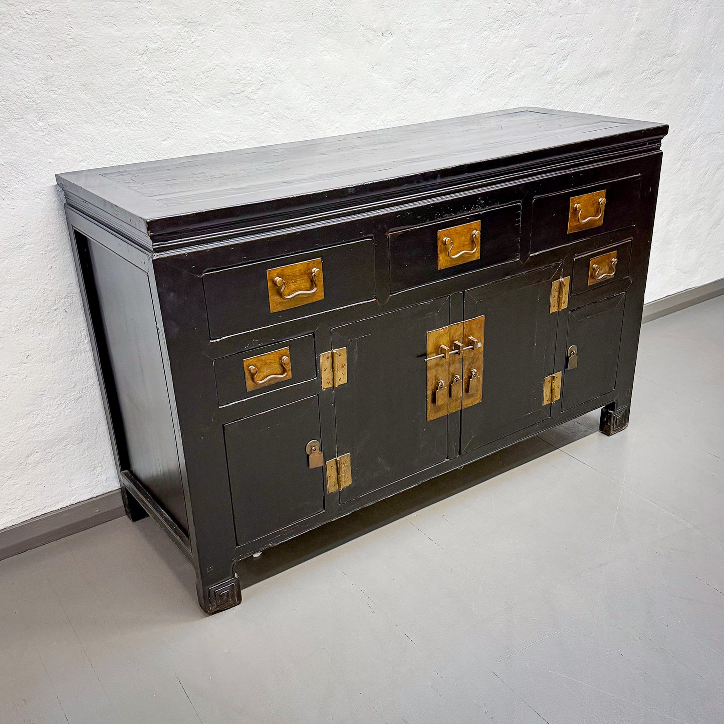 Dark wooden sideboard with gold accents on a white floor and light gray wall.