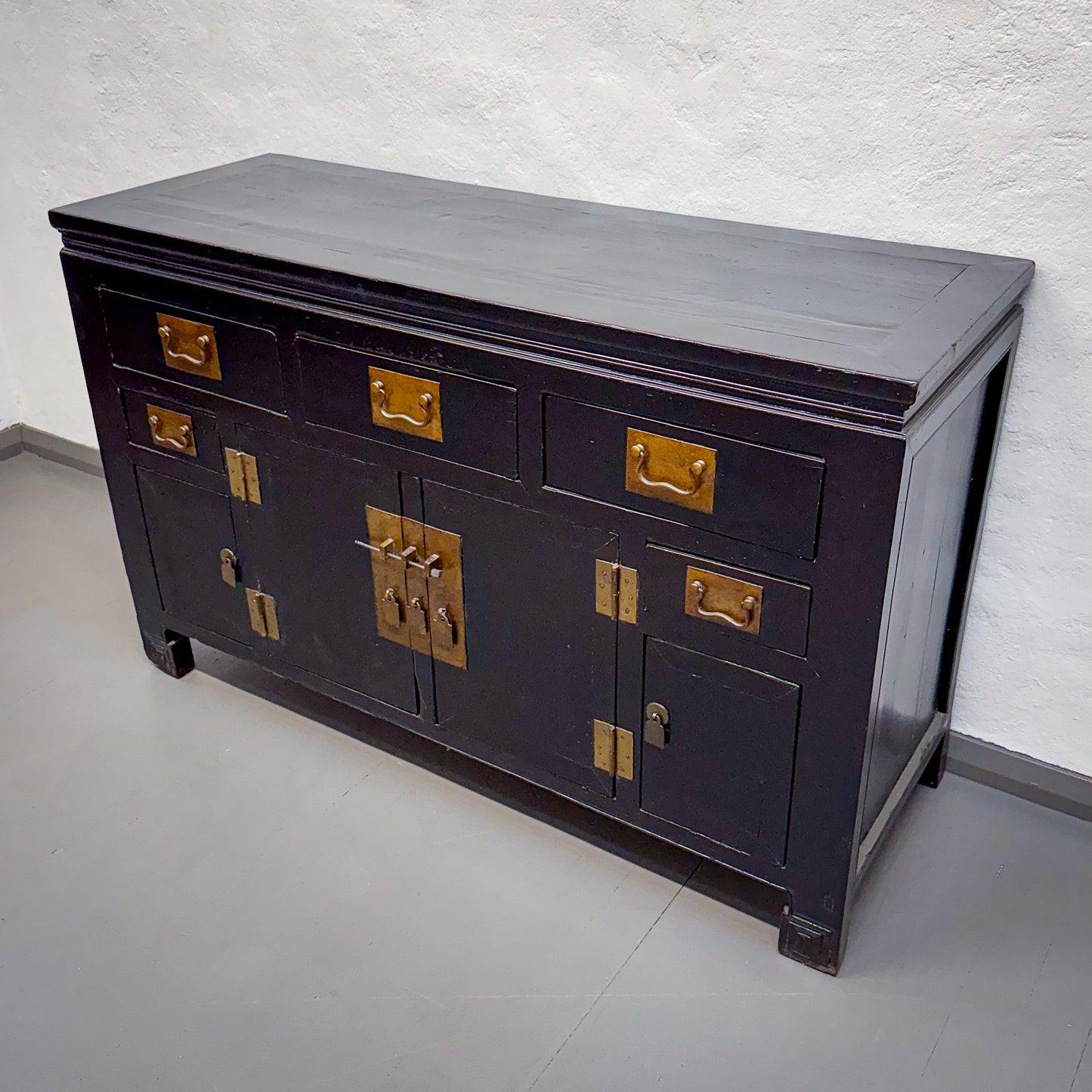 Dark wooden cabinet with gold hardware on a white floor and wall