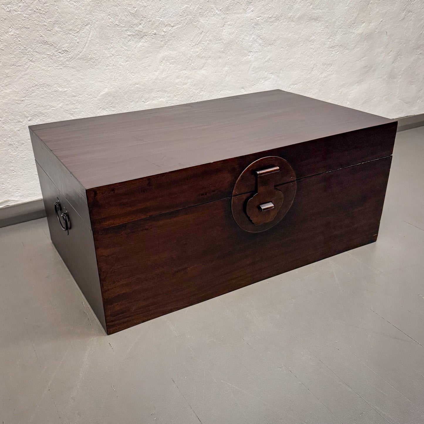 Wooden box with a round handle on a light gray floor.