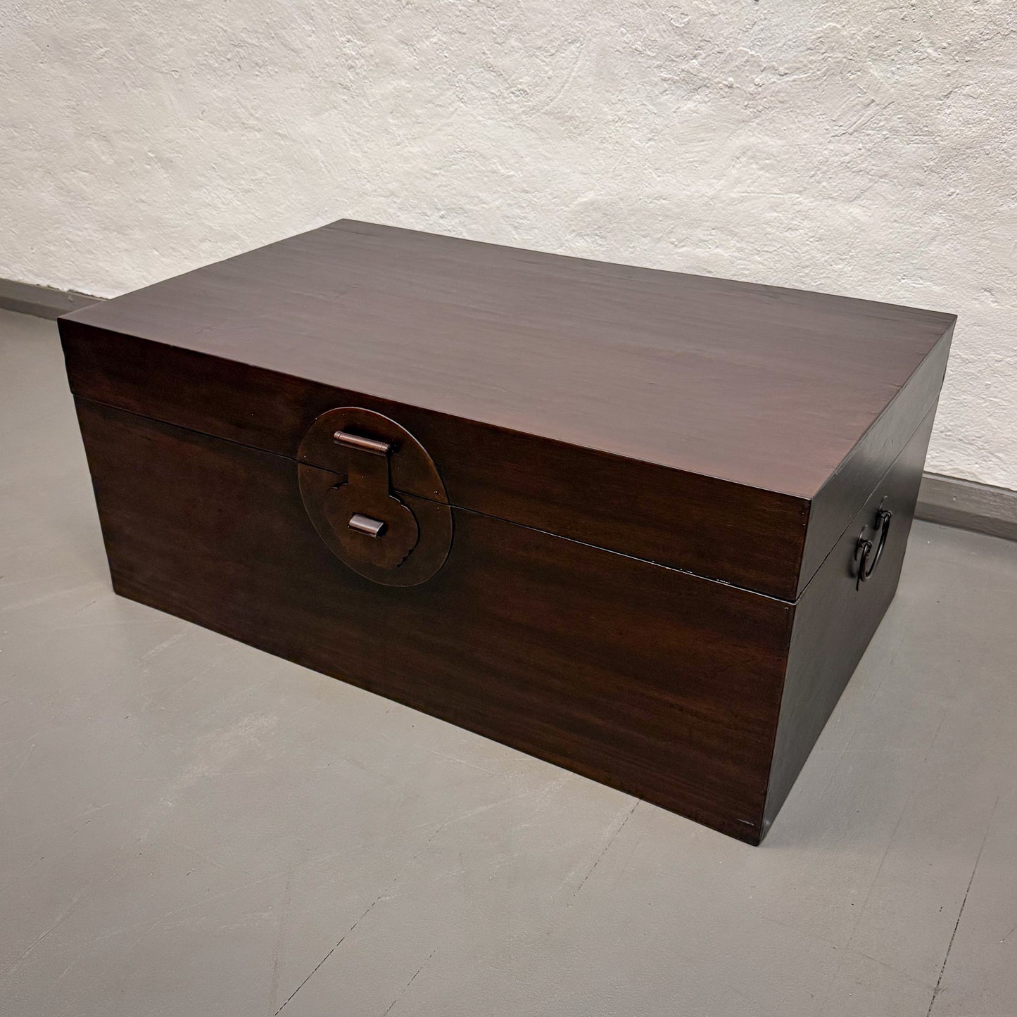 Wooden chest with a circular handle on a light gray floor.