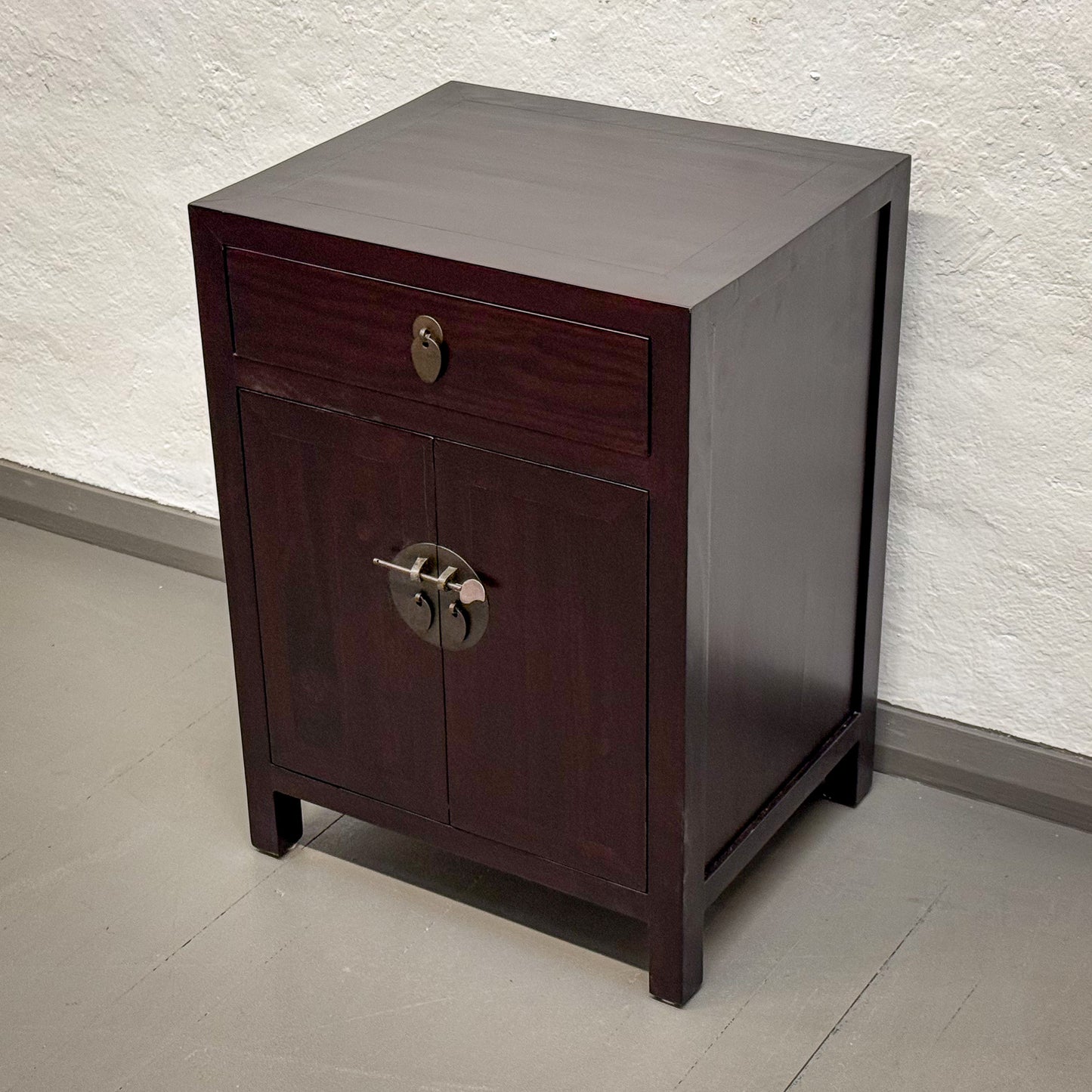 Wooden side table with a drawer and cabinet against a neutral wall.