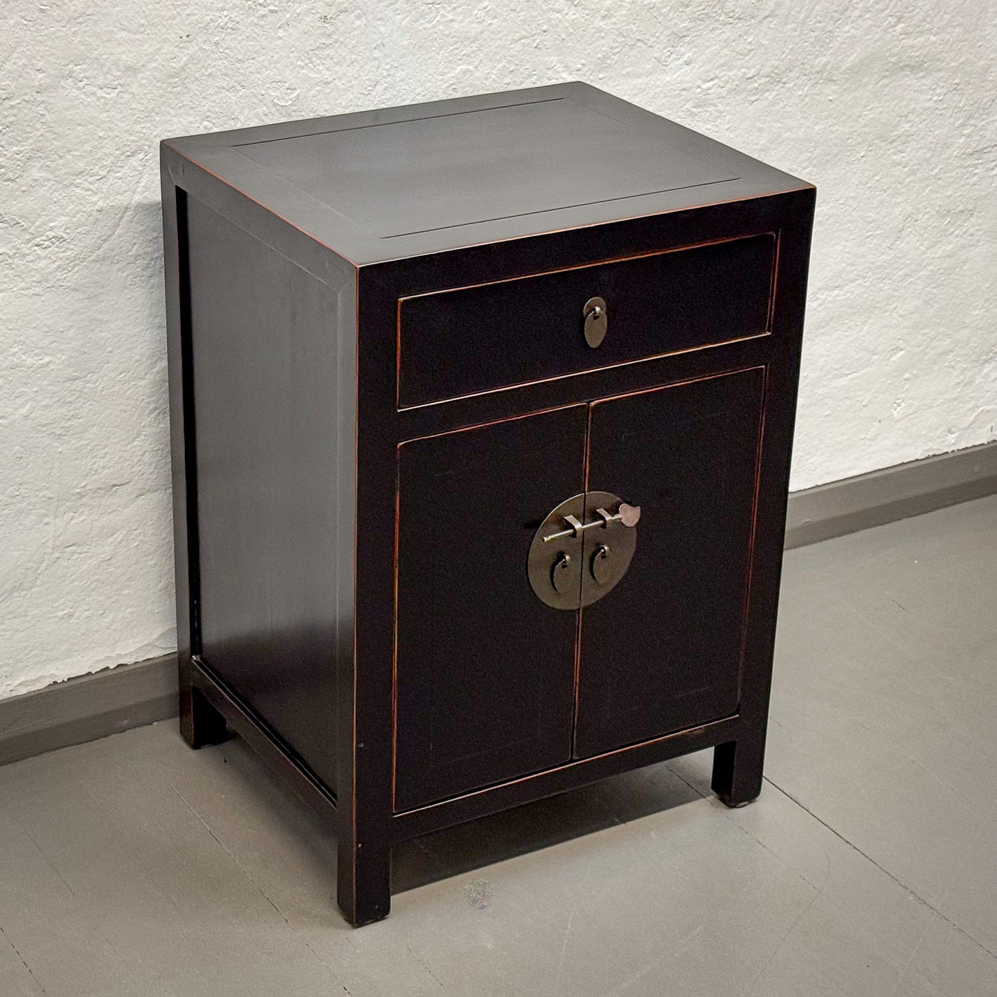 Dark wooden nightstand with a single drawer and decorative handle on a plain floor.