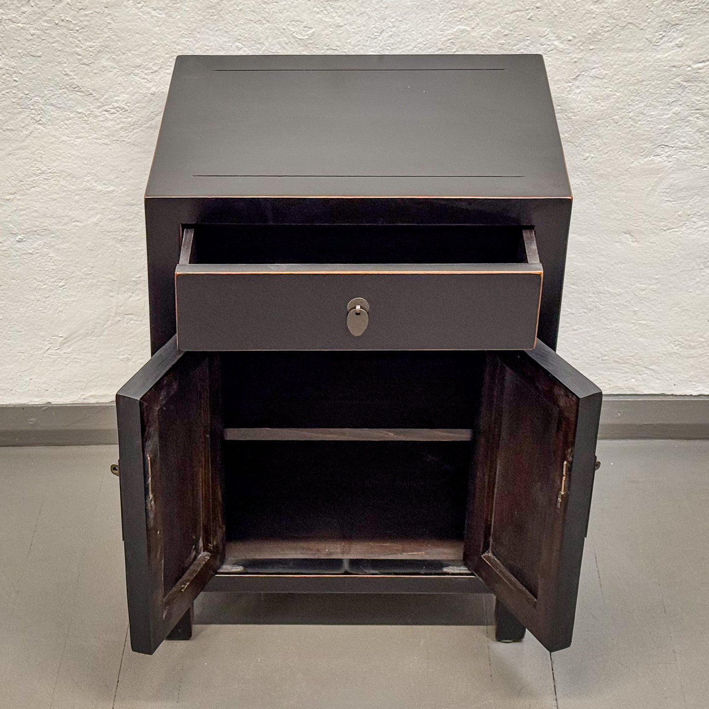 Dark wooden side table with a drawer and open doors against a light background