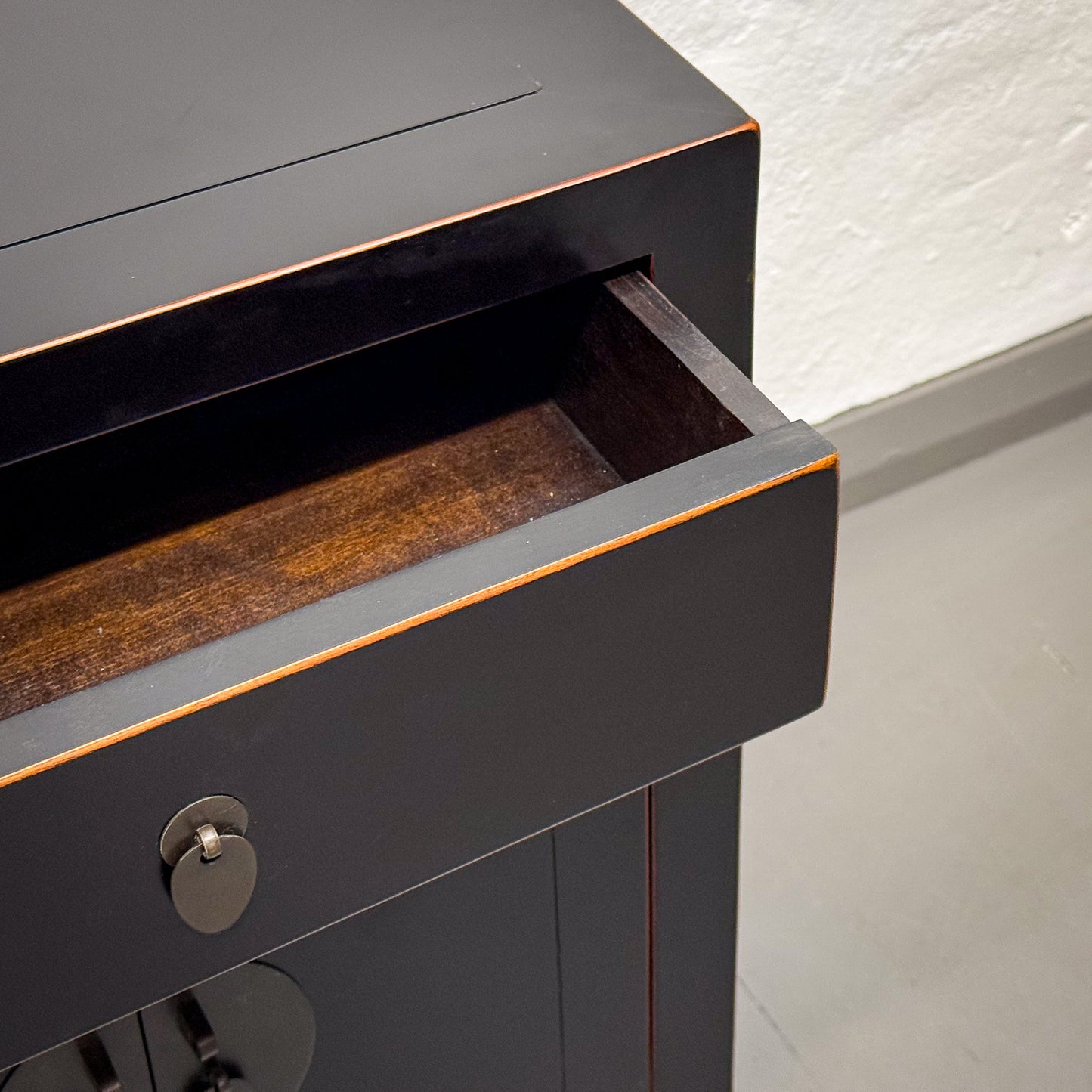 Black cabinet with an open drawer on a light gray floor.