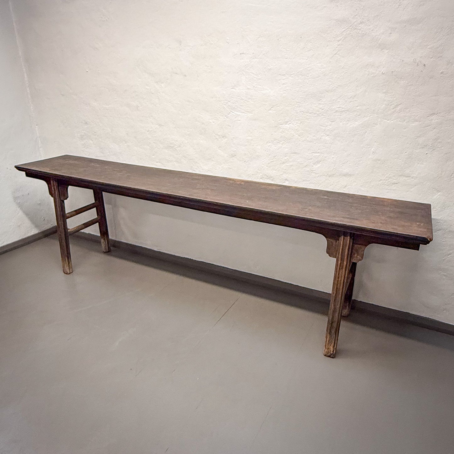 Long wooden bench against a white textured wall.
