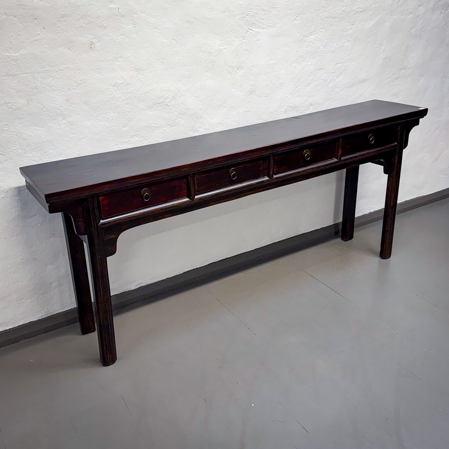 Long dark wooden table with drawers against a white wall.