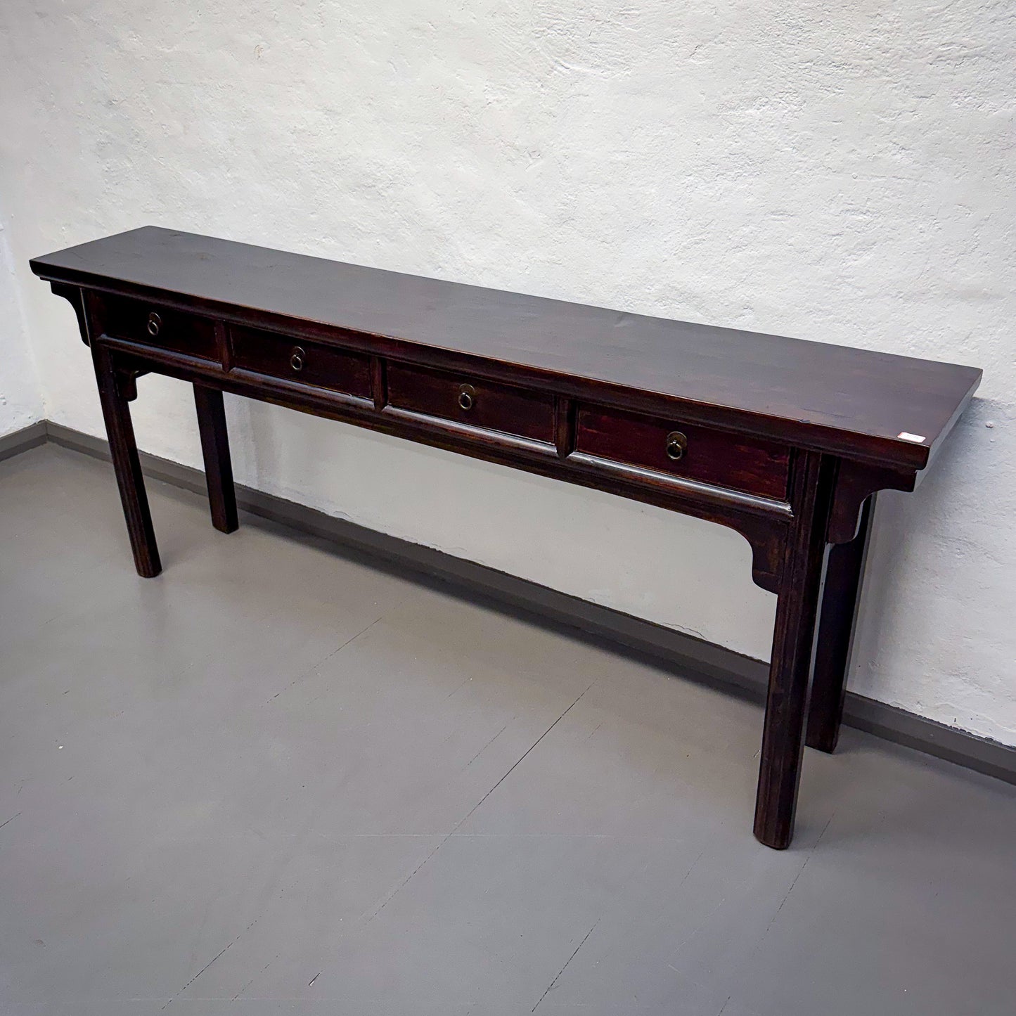 Long dark wooden table against a white brick wall.