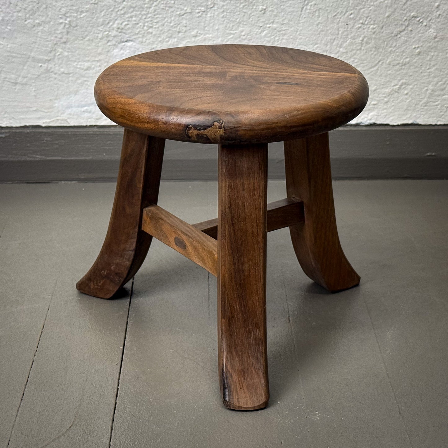Wooden stool with a worn finish on a plain floor.