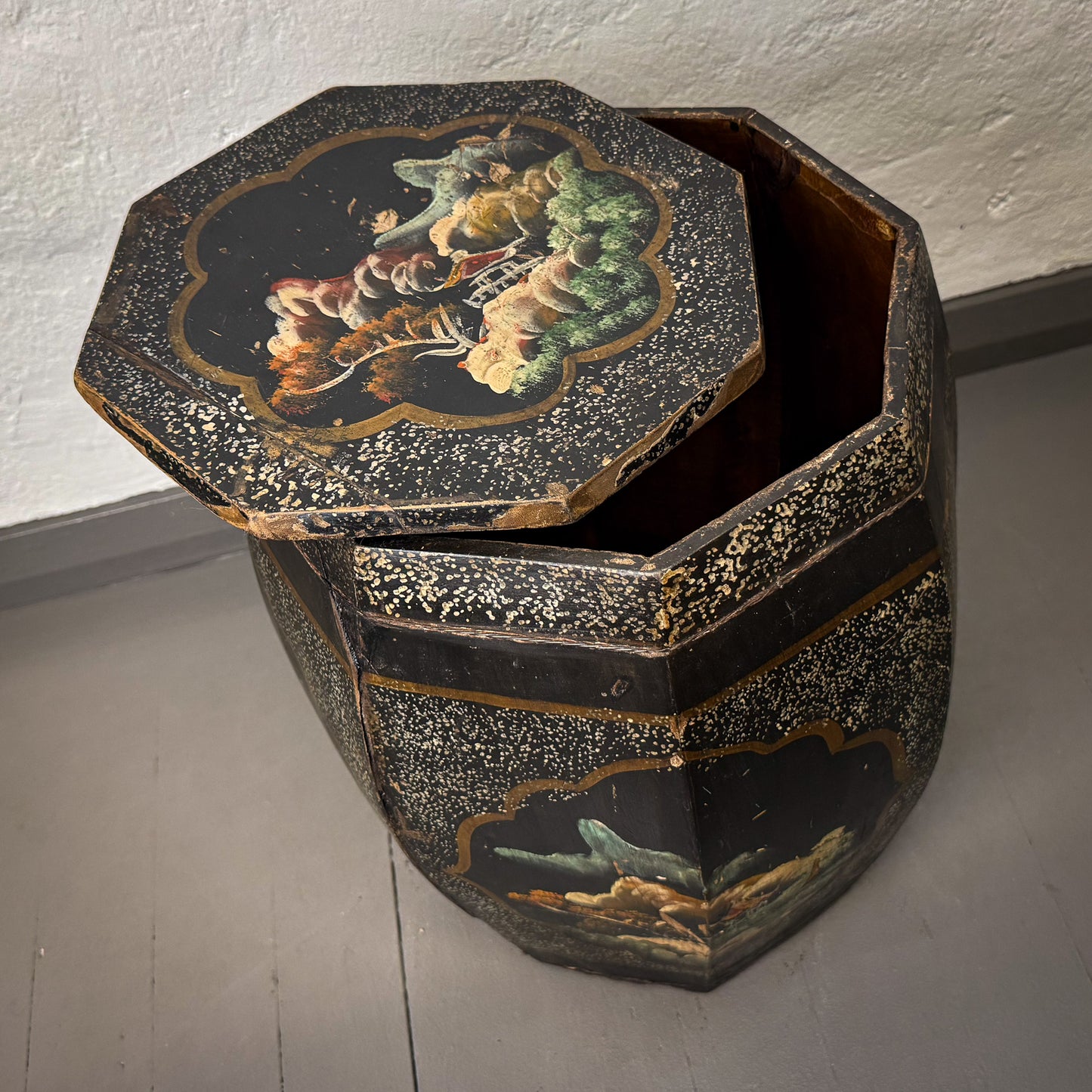 Decorative hexagonal box with painted lid on a plain floor.