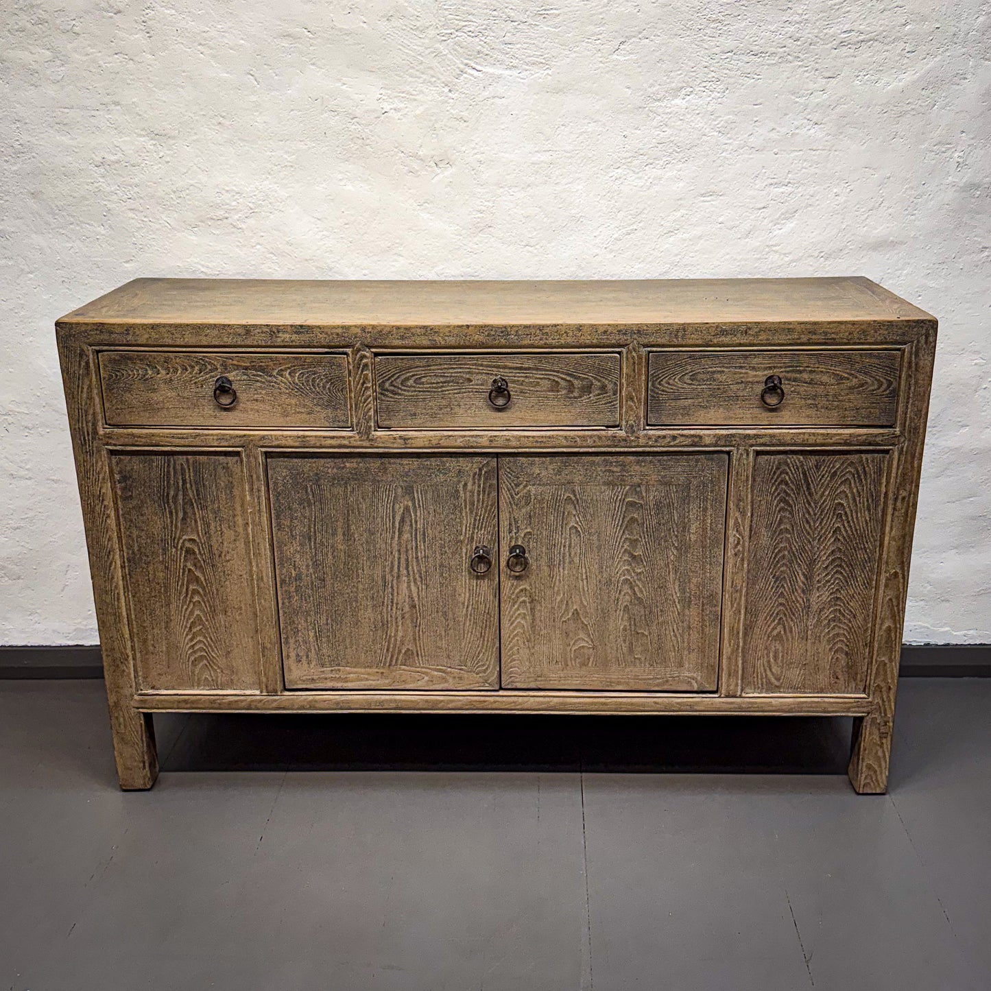 Wooden sideboard with four drawers and four doors against a white brick wall.