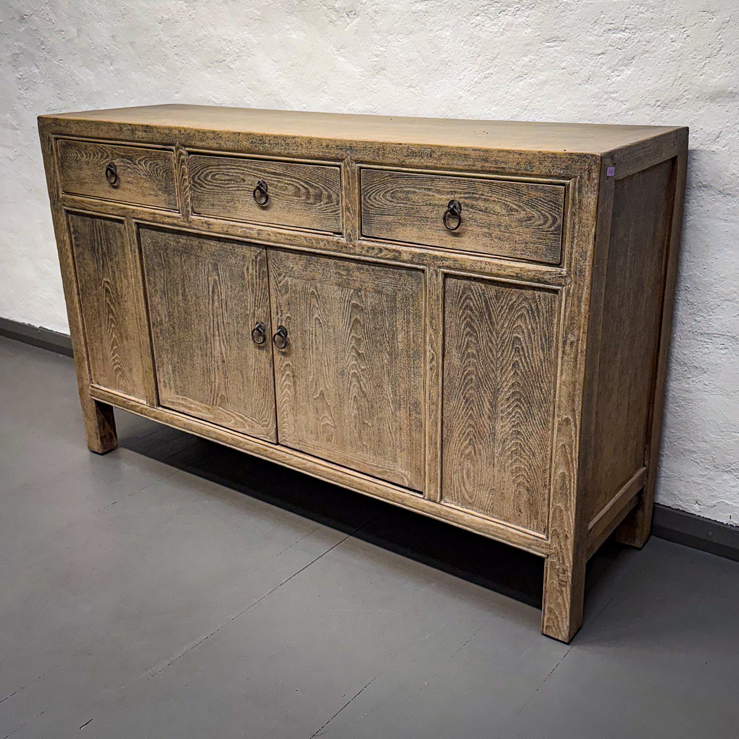 Wooden sideboard with drawers and doors against a textured wall.