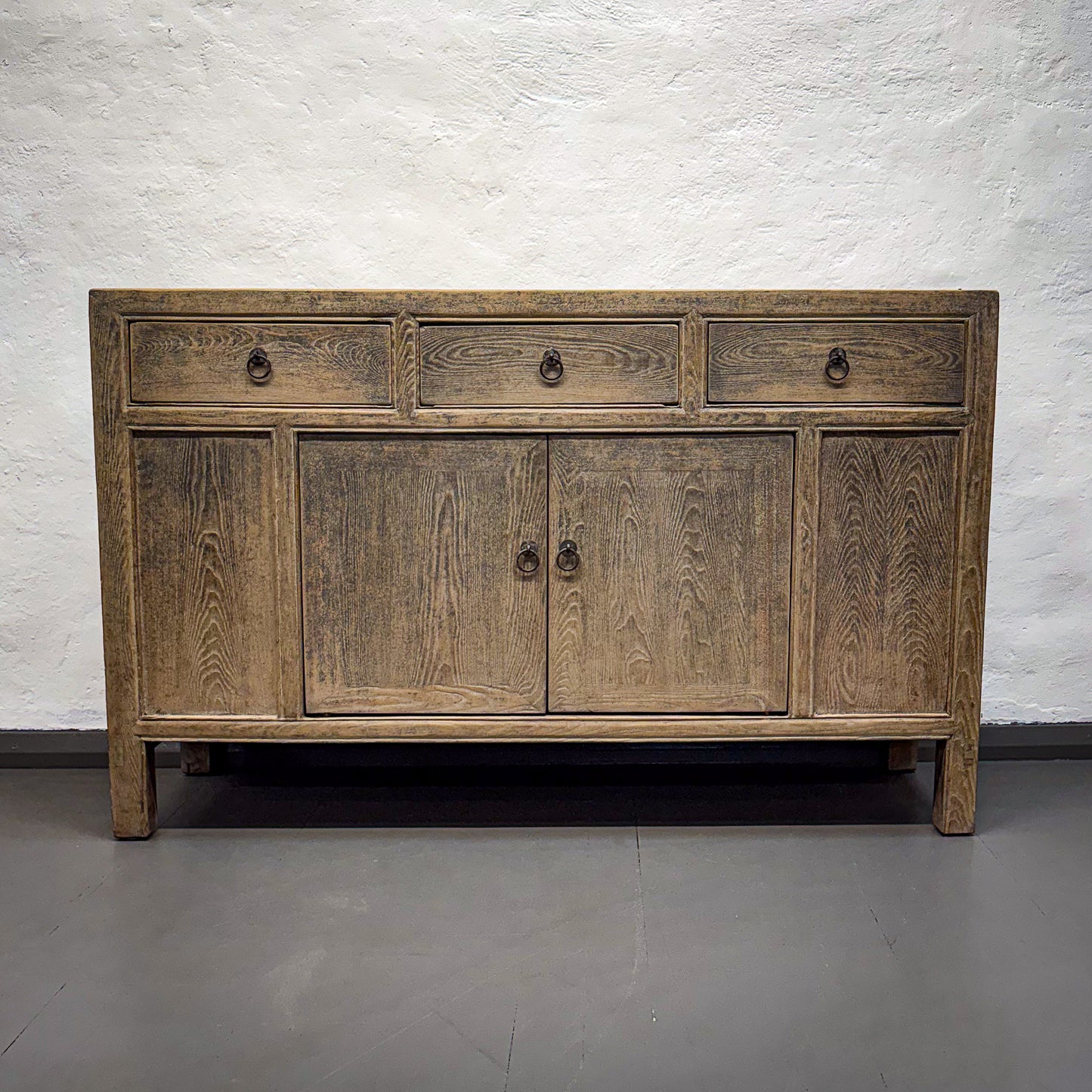 Wooden sideboard with three drawers and four doors against a white brick wall.