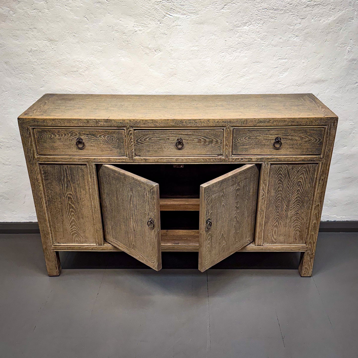 Wooden sideboard with open doors against a white brick wall.
