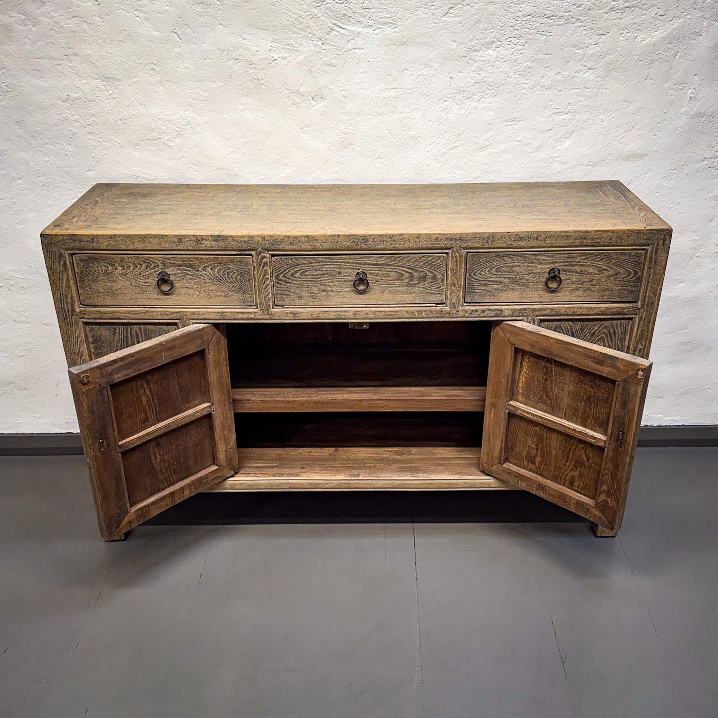 Wooden sideboard with open doors against a plain wall.