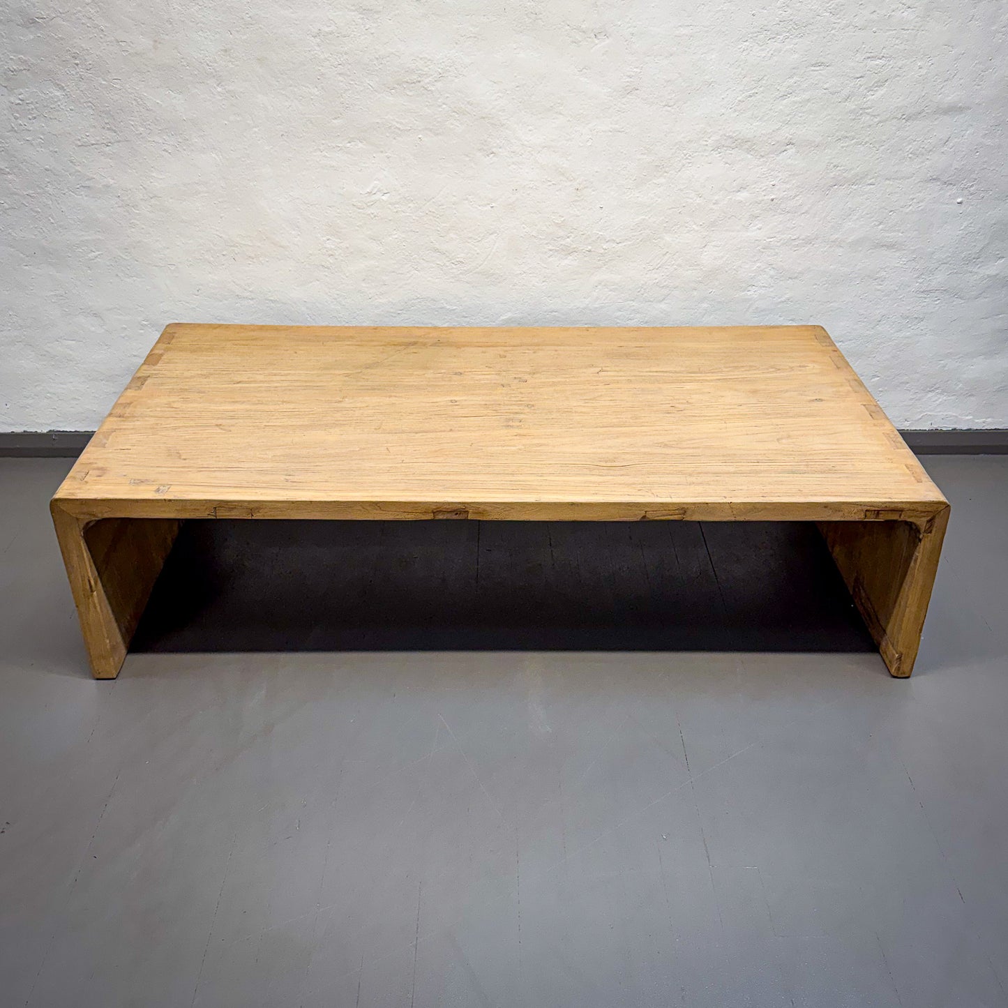 Wooden coffee table against a textured white wall.