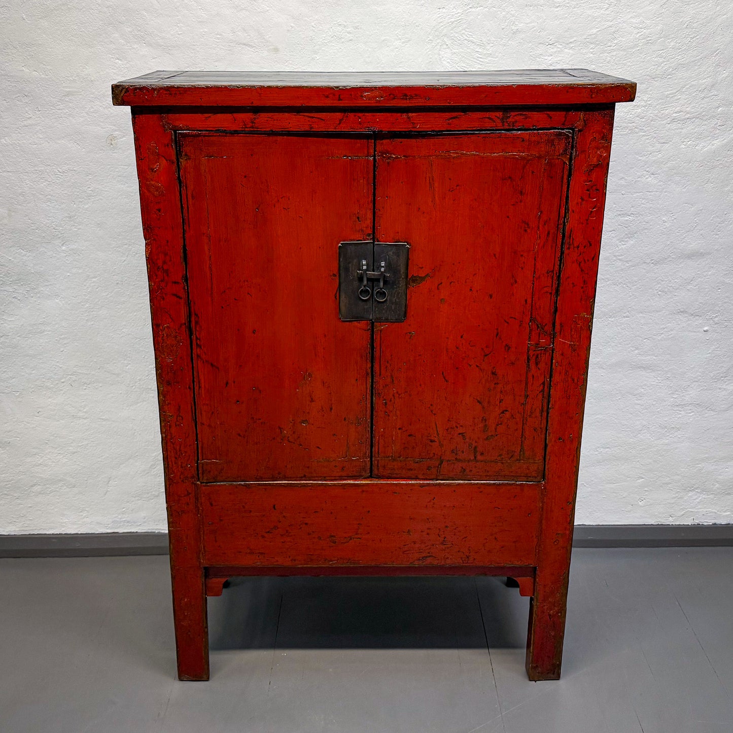 Red wooden cabinet with a textured surface on a gray floor and white wall background