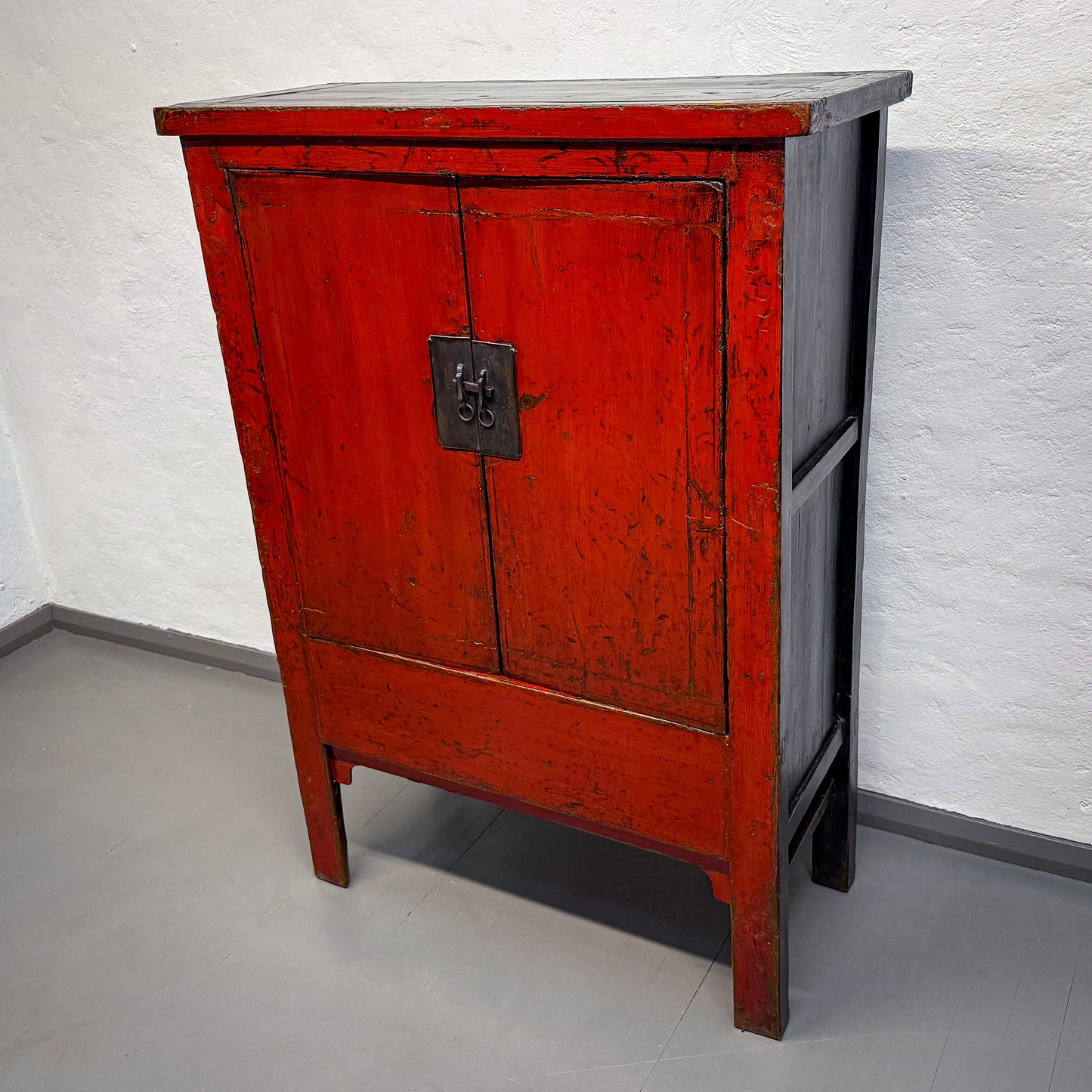Red wooden cabinet with a gray top against a white textured wall.
