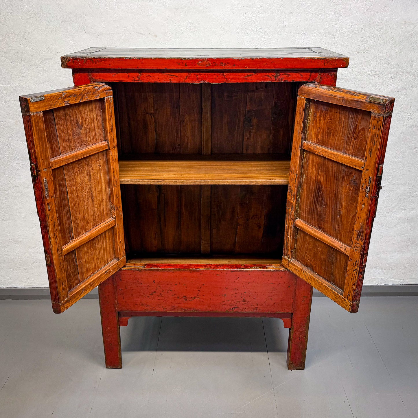 Wooden cabinet with open doors on a gray floor and white wall background