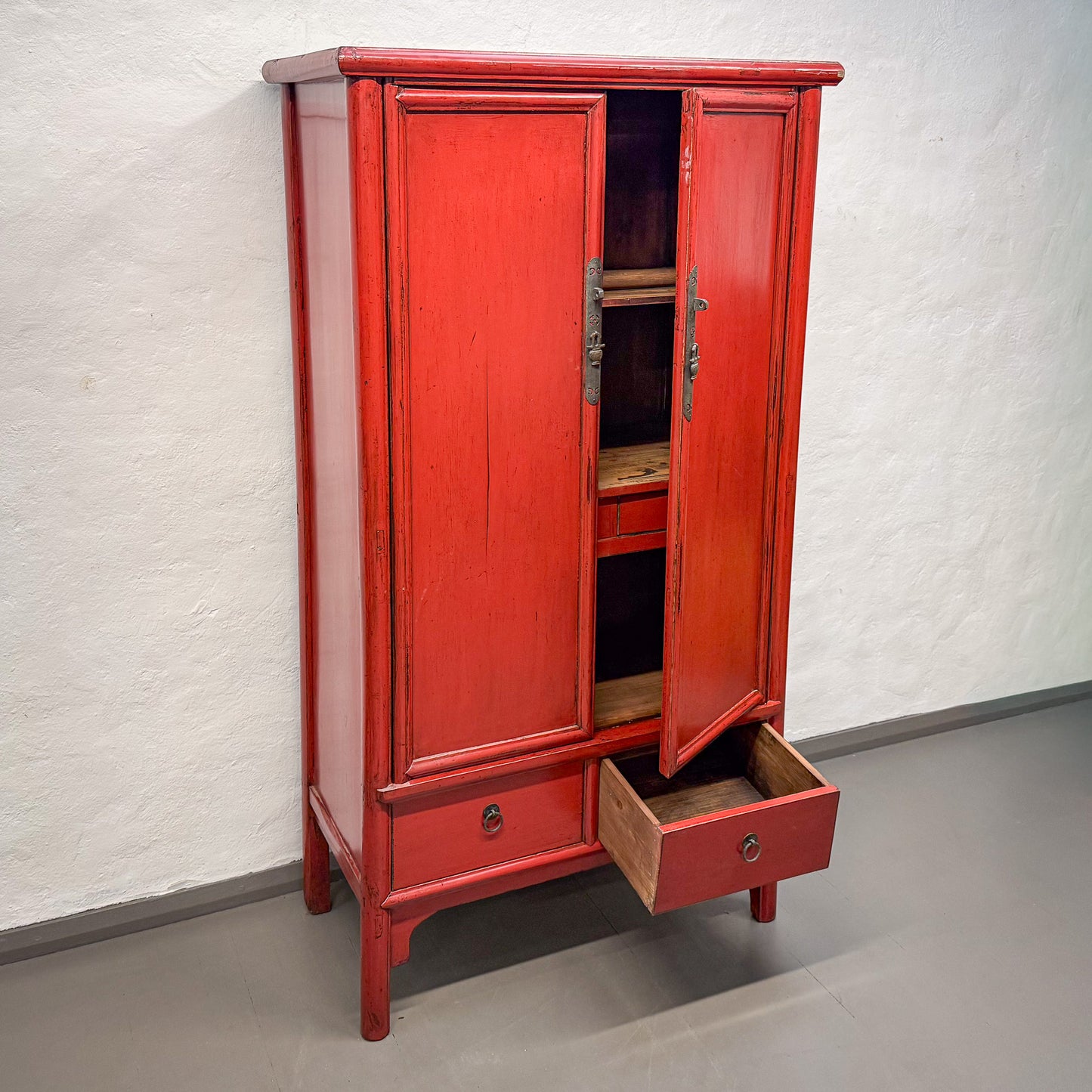 Red wooden cabinet with open doors on a gray floor against a white wall
