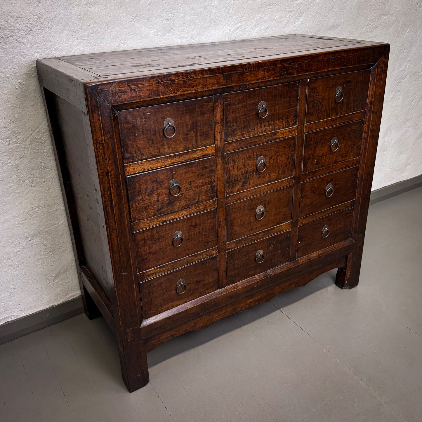 Wooden dresser with multiple drawers against a textured wall.