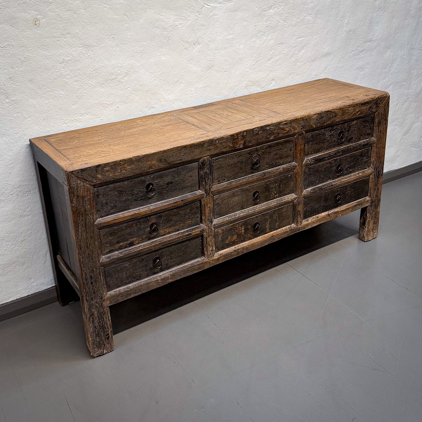 Wooden dresser with multiple drawers against a white brick wall.