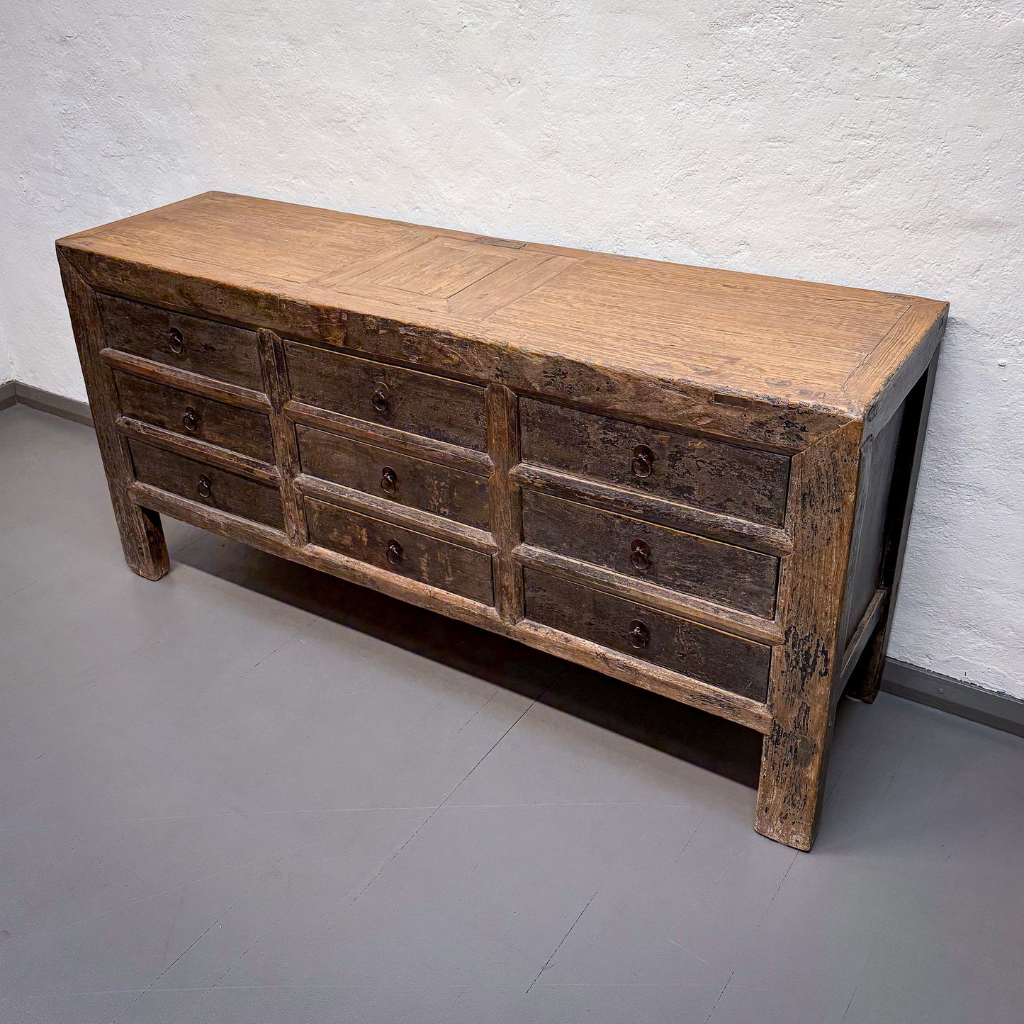 Wooden dresser with multiple drawers against a white brick wall.