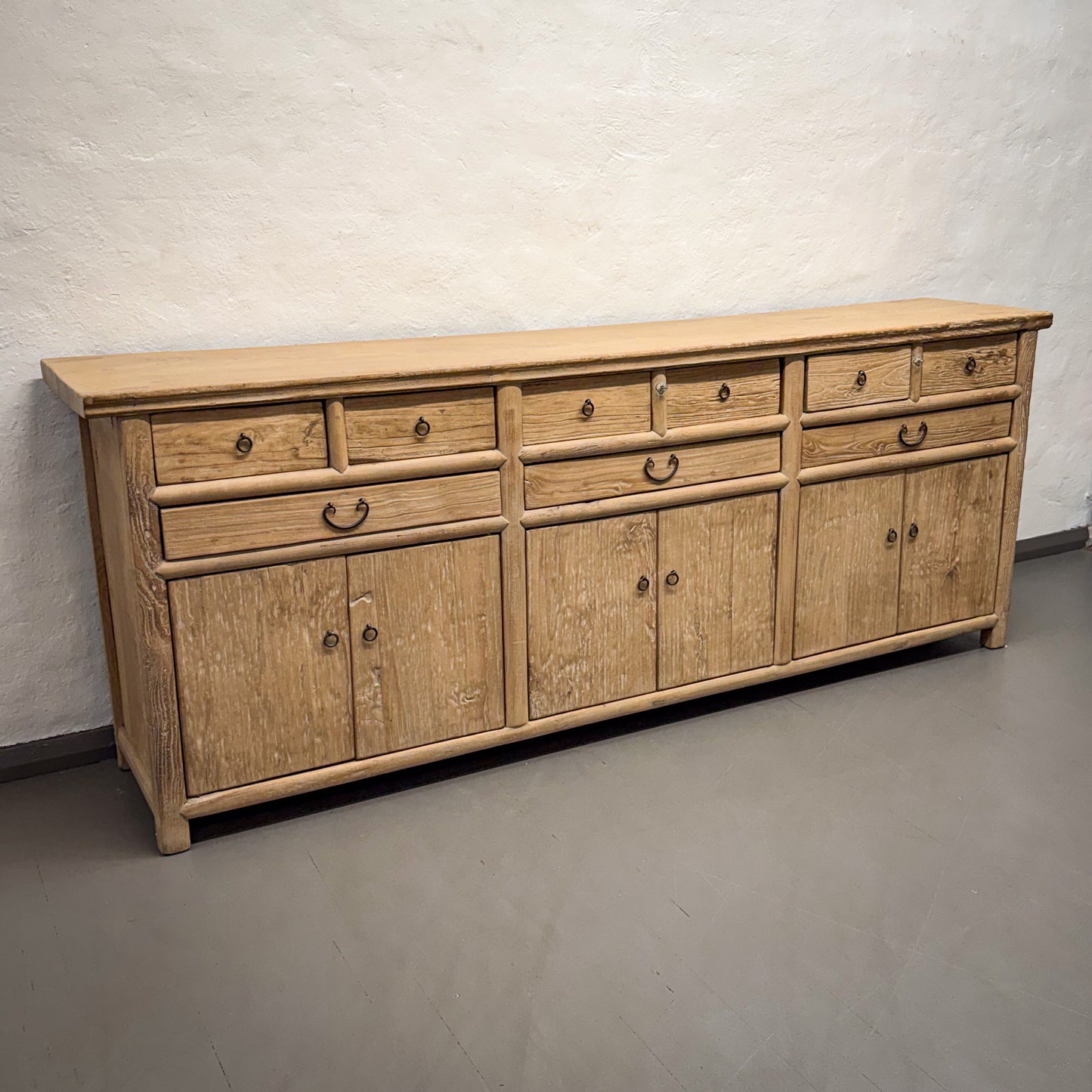 Wooden sideboard with multiple drawers and doors against a plain wall.