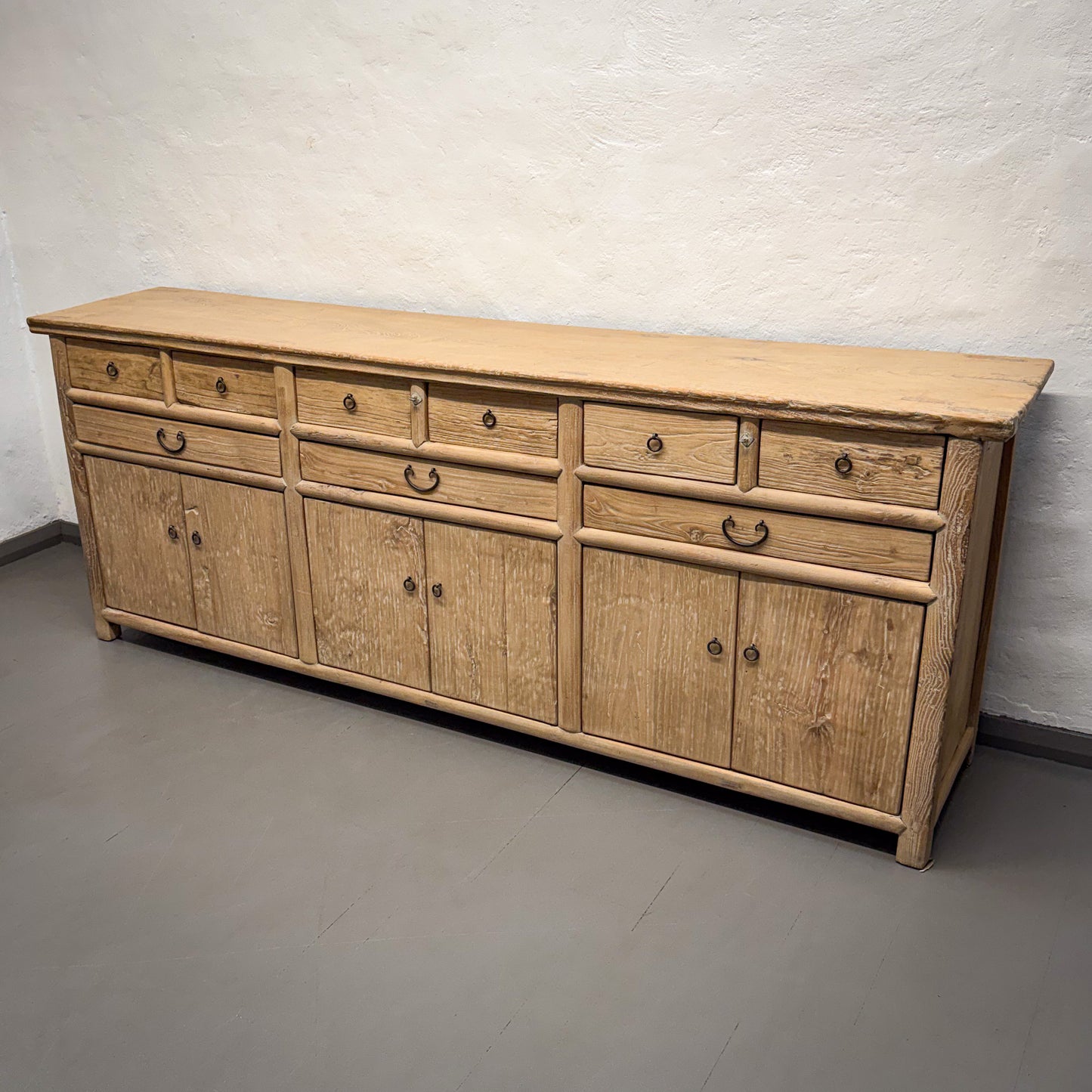 Wooden sideboard with multiple drawers and doors against a plain wall.