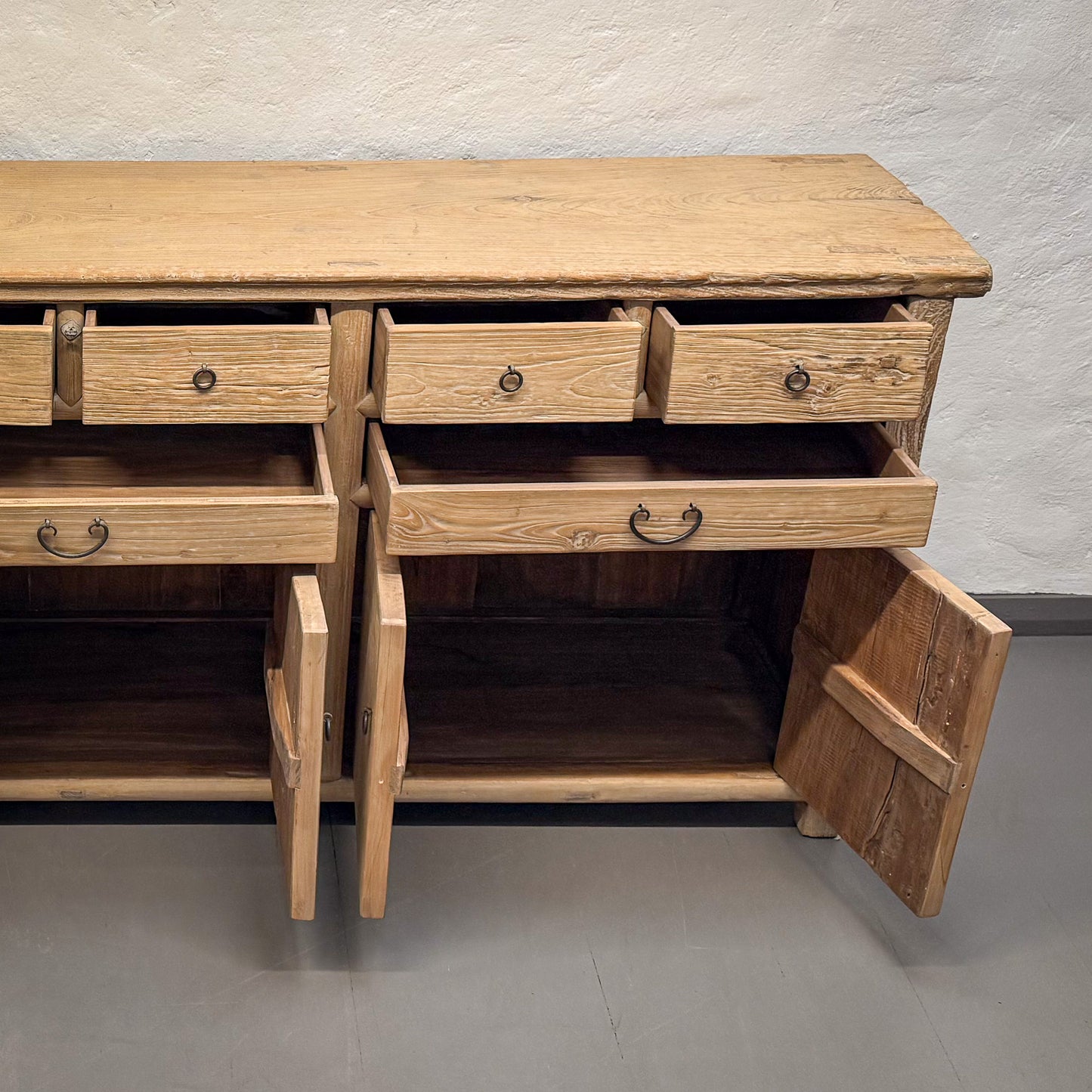 Wooden sideboard with open drawer against a plain wall.