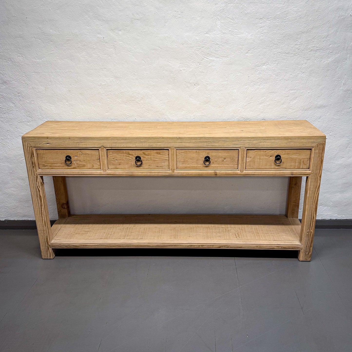 Wooden console table with four drawers against a plain wall.