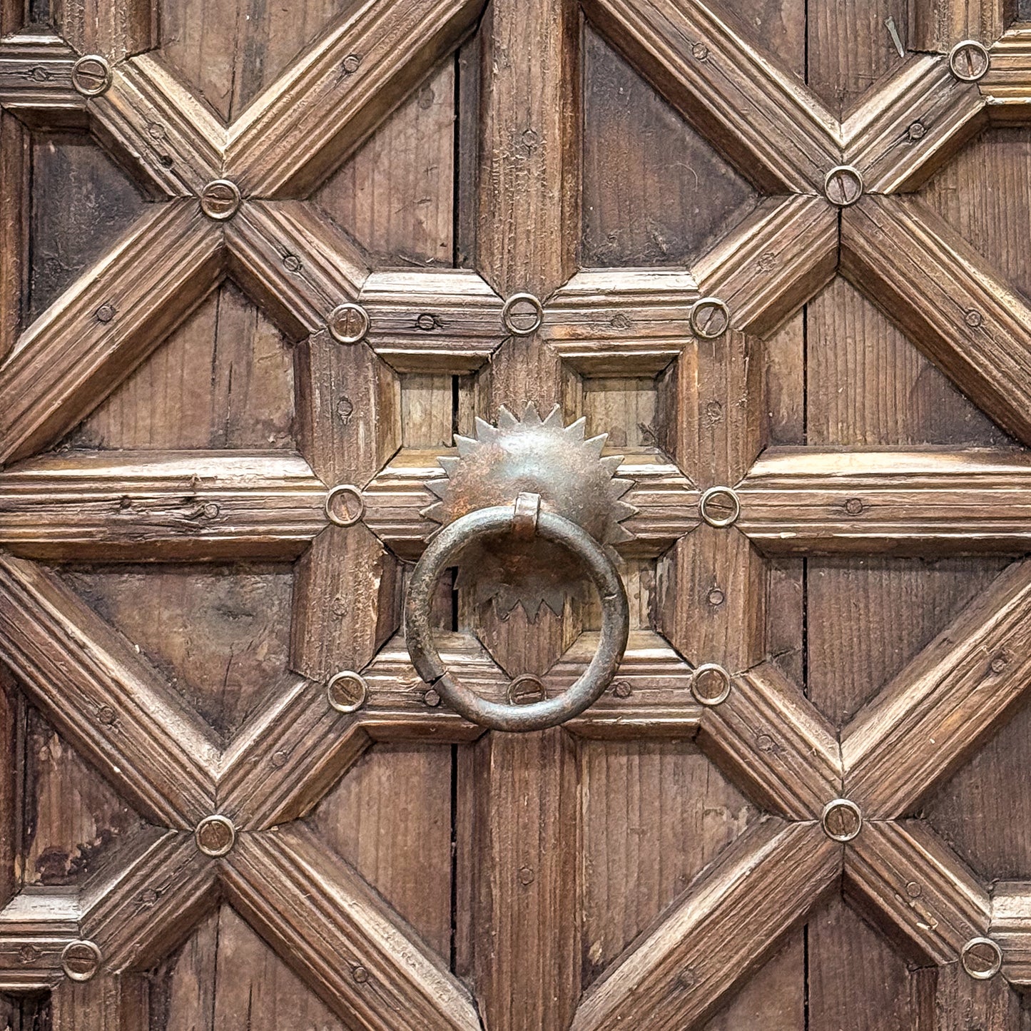 Close-up of a wooden door with geometric patterns and a metal knocker.